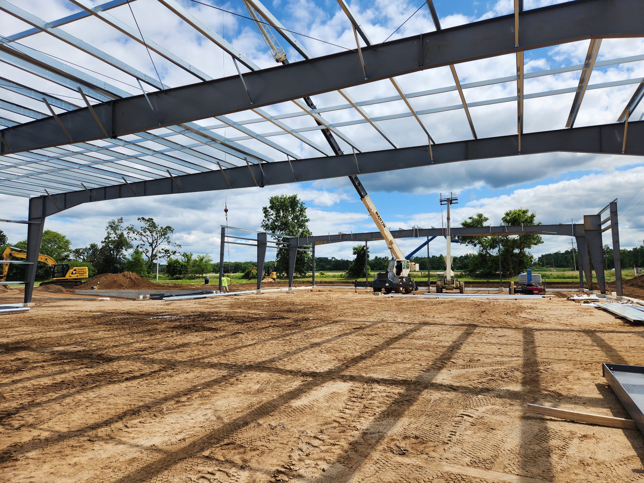 Construction site with steel framework and crane under a blue sky.