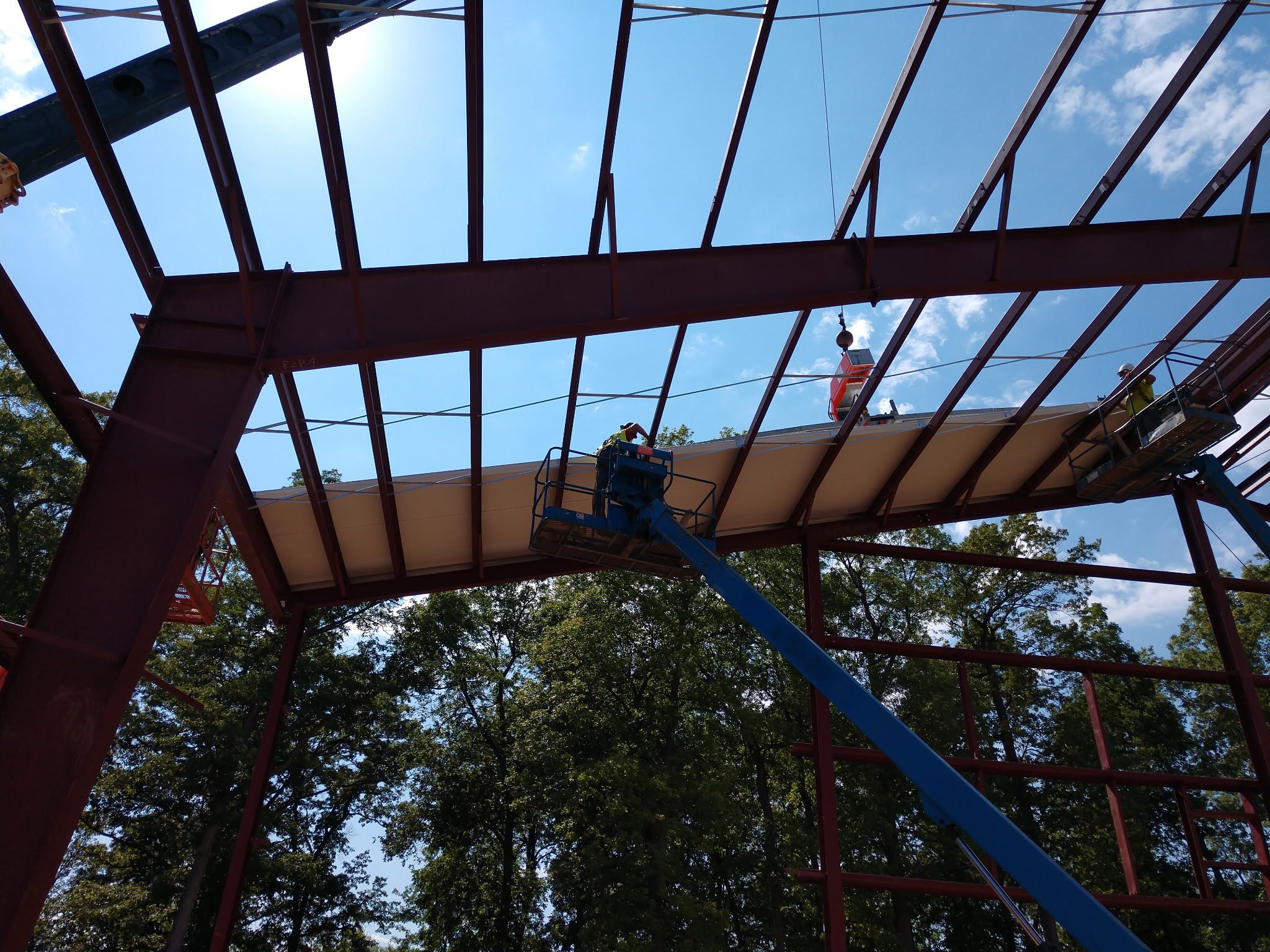 Worker on lift installing roof panels on steel frame structure outdoors.