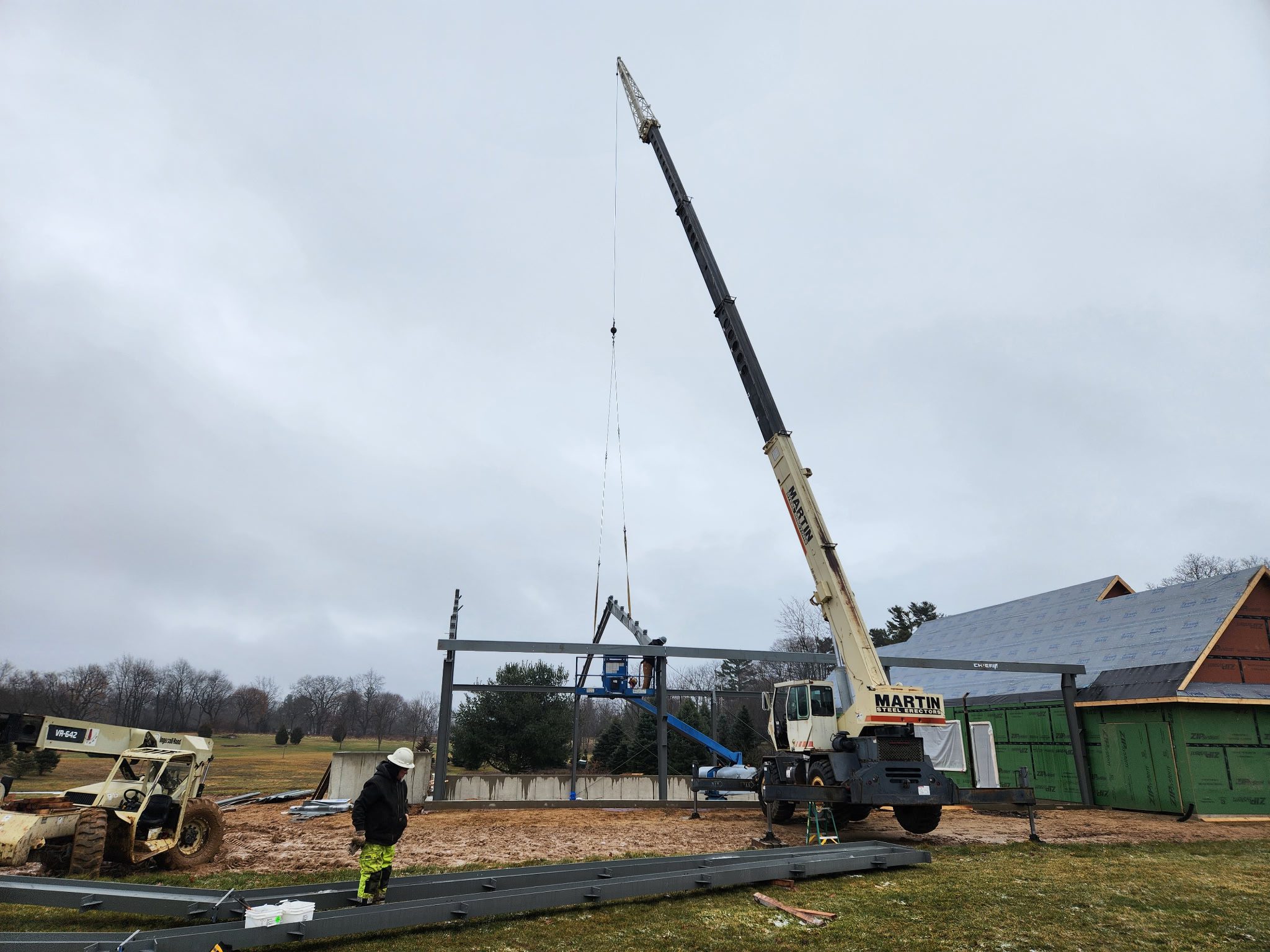 A crane lifting a steel beam at a construction site on a cloudy day.