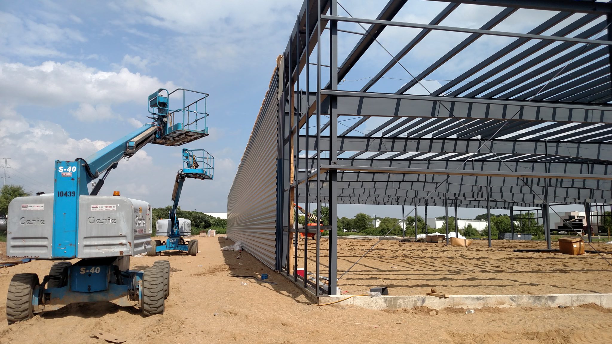 Construction site with metal framework and workers on lifts.