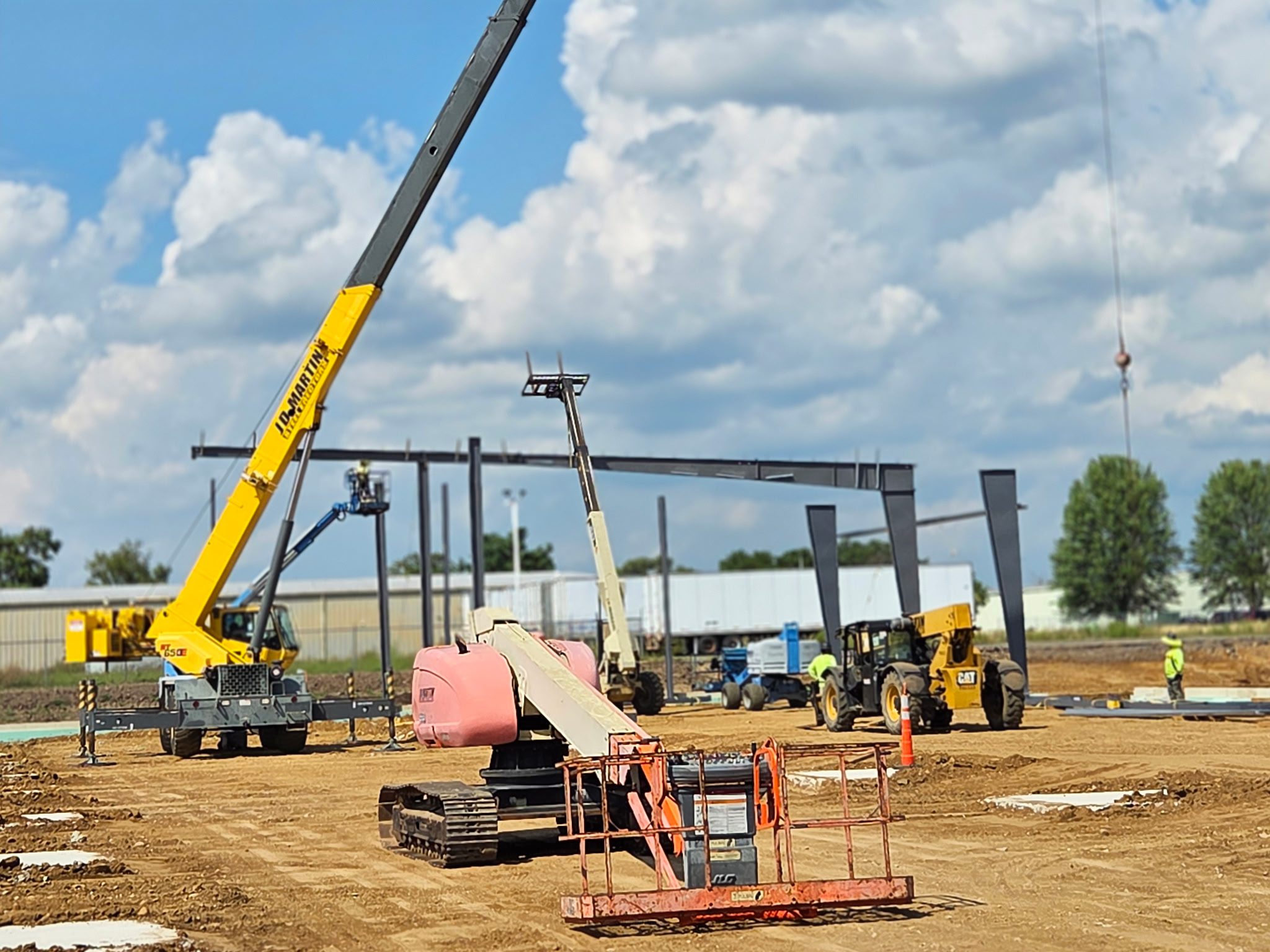 Construction site with cranes and steel framework under a cloudy sky.