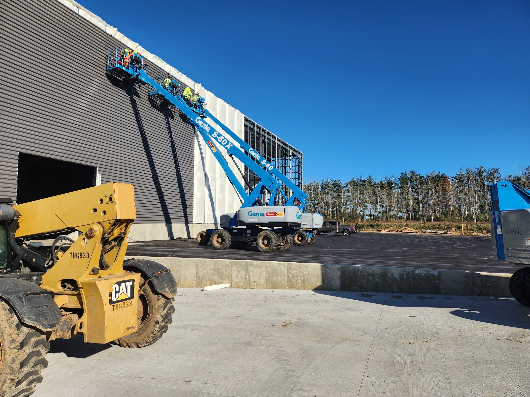 Construction equipment operating near a concrete wall under a clear blue sky.