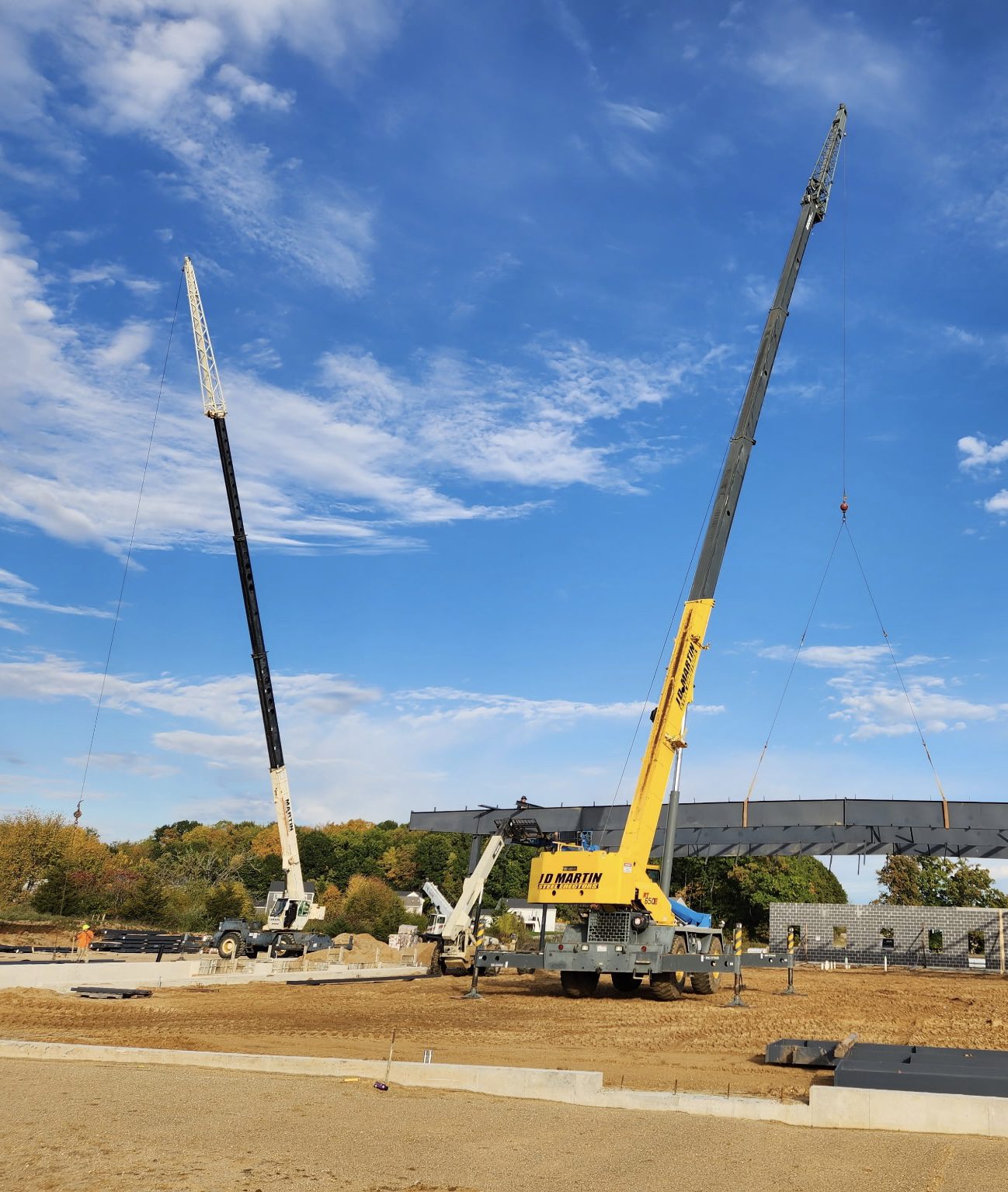 Two cranes lifting heavy materials on a construction site under a blue sky.