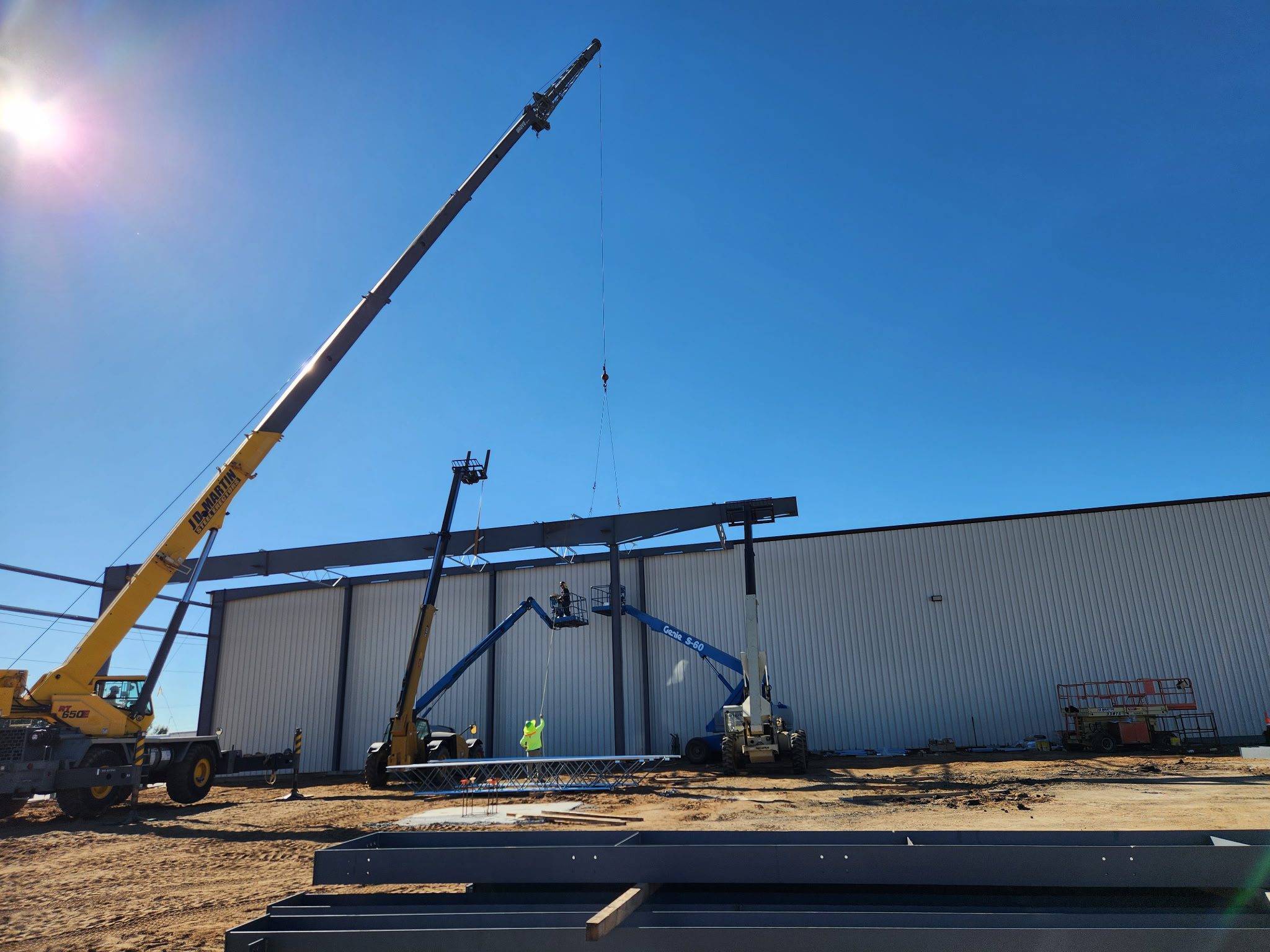 Crane lifting steel beams at a construction site under a clear blue sky.