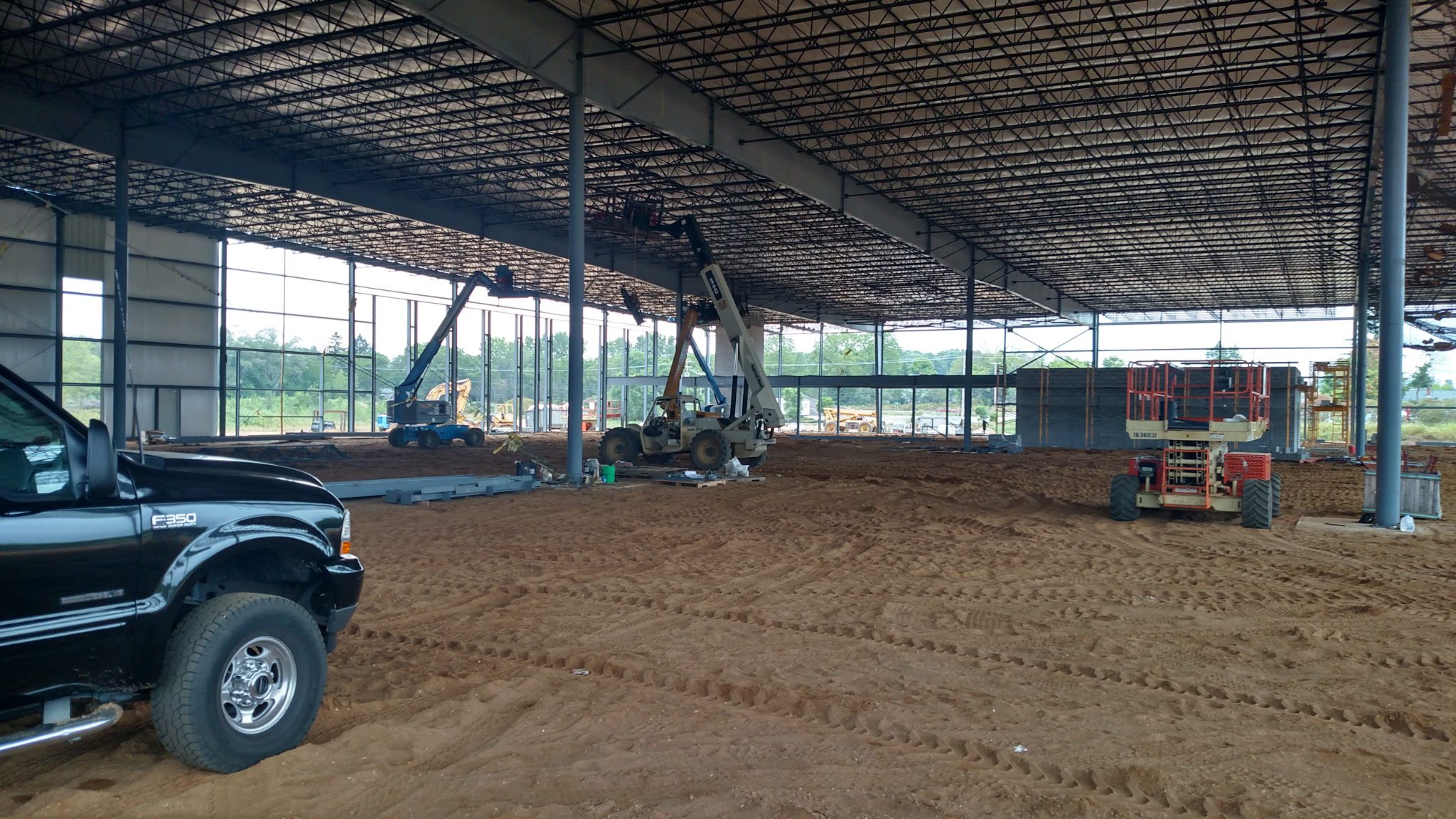 Construction site inside a large building with machinery and dirt ground.