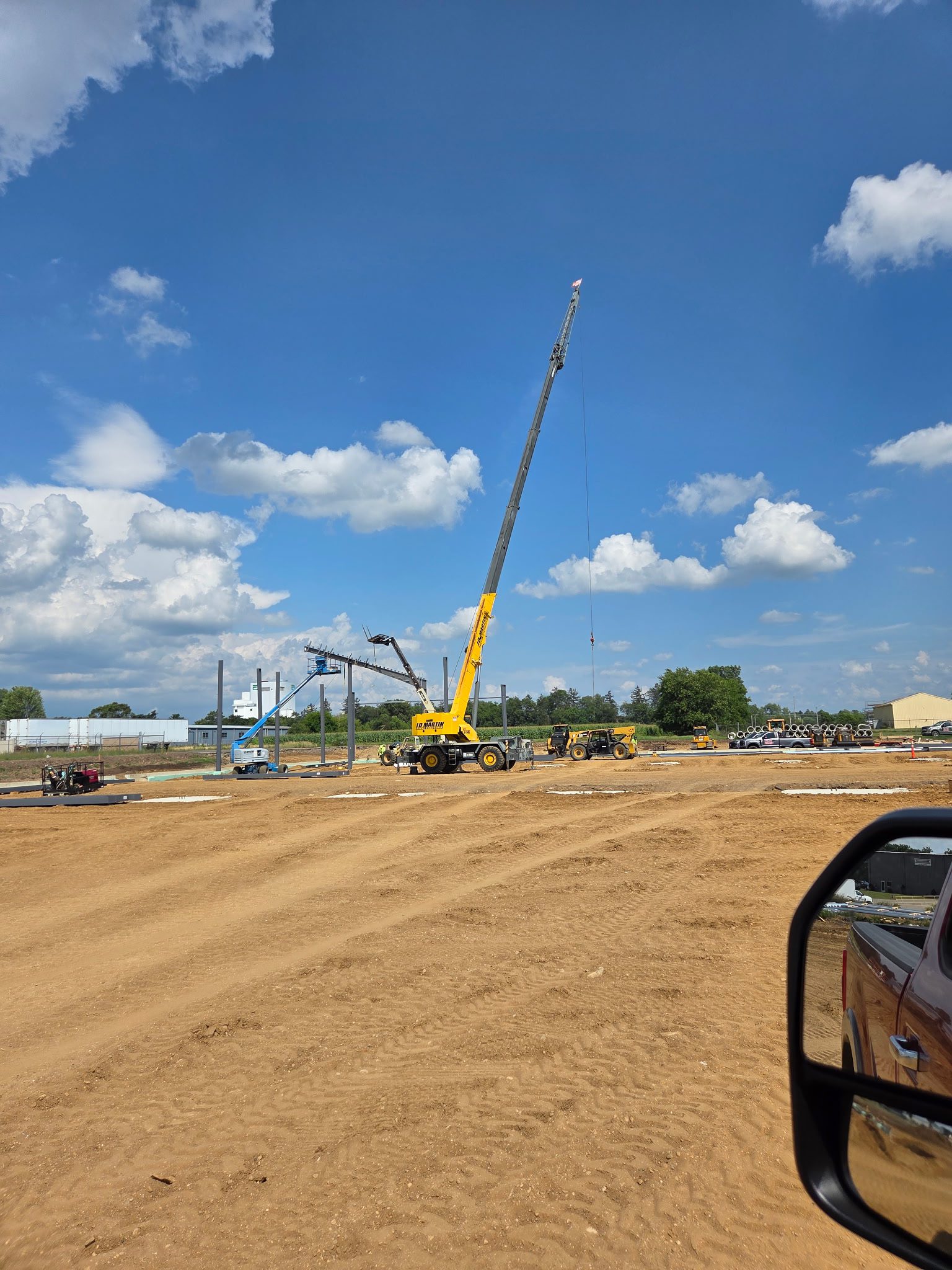 A yellow crane operates on a construction site under a blue sky.
