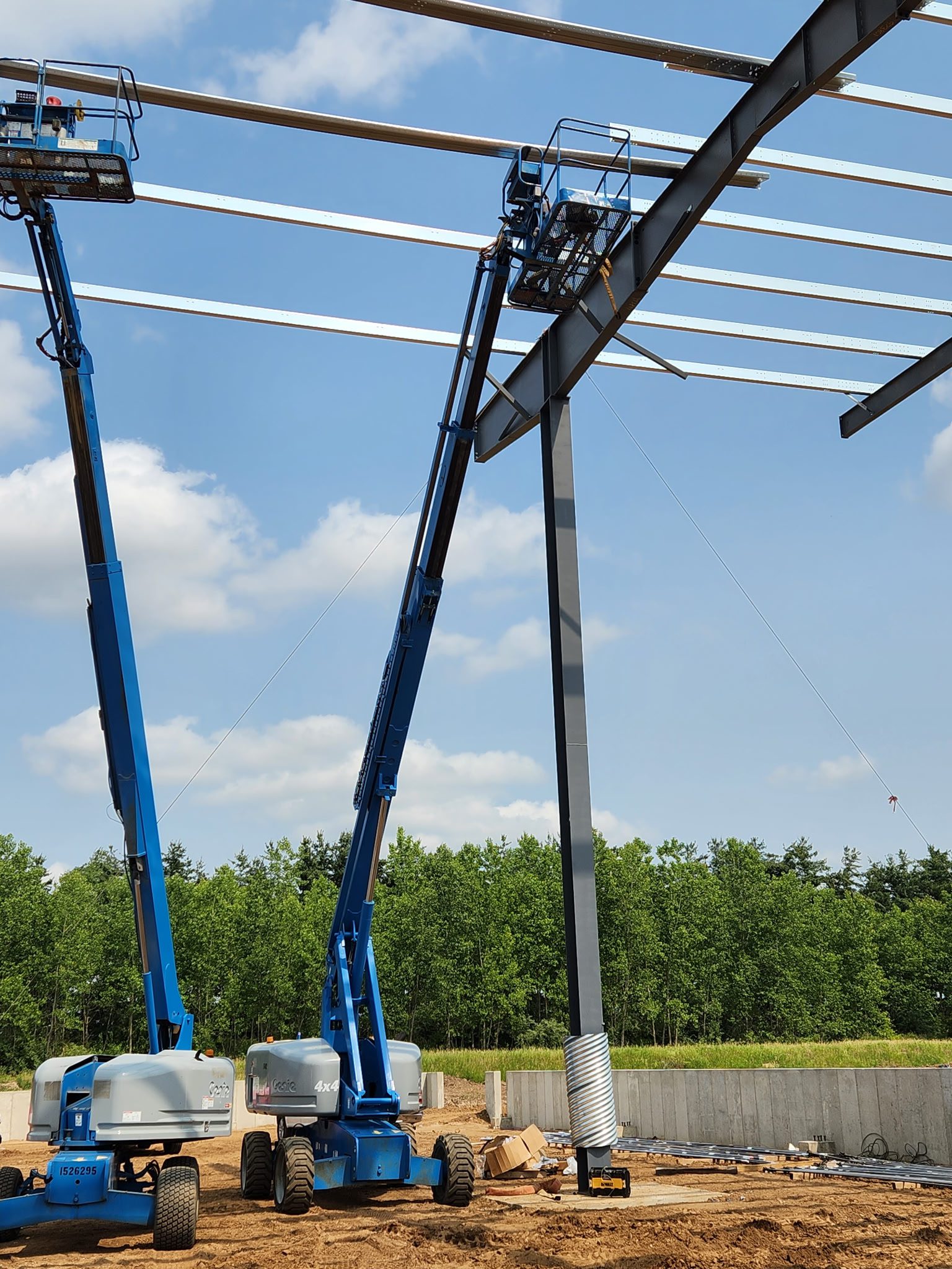 Two blue boom lifts extended high against a blue sky with clouds.