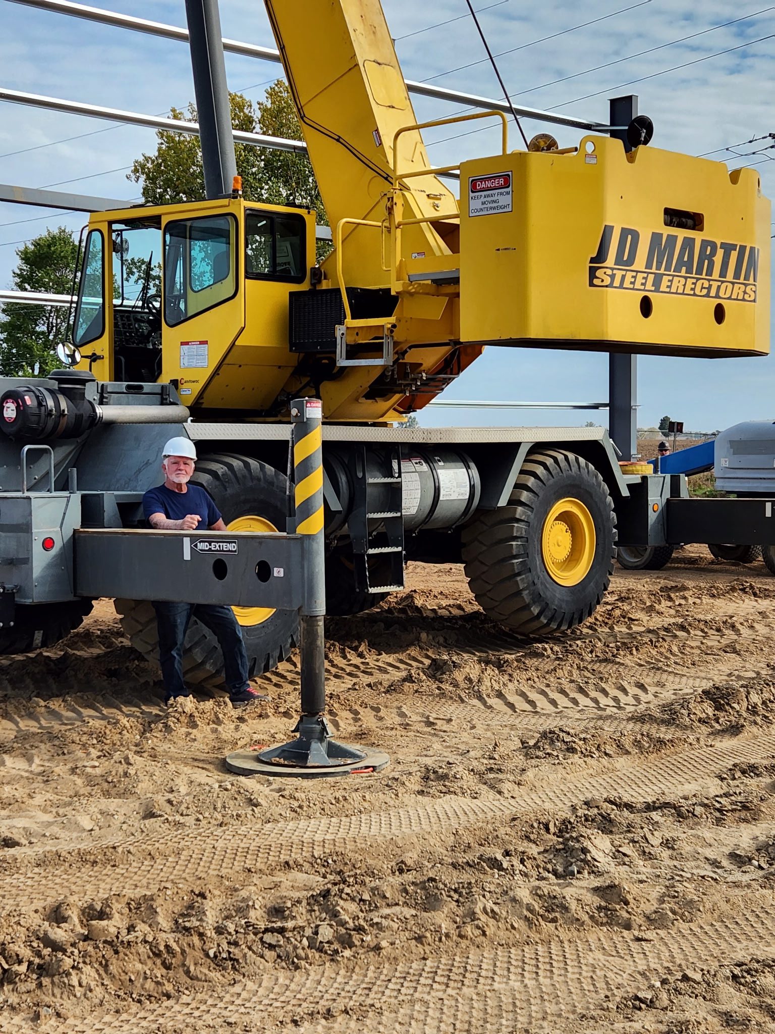 Yellow construction crane stabilizing on dirt ground at a worksite.