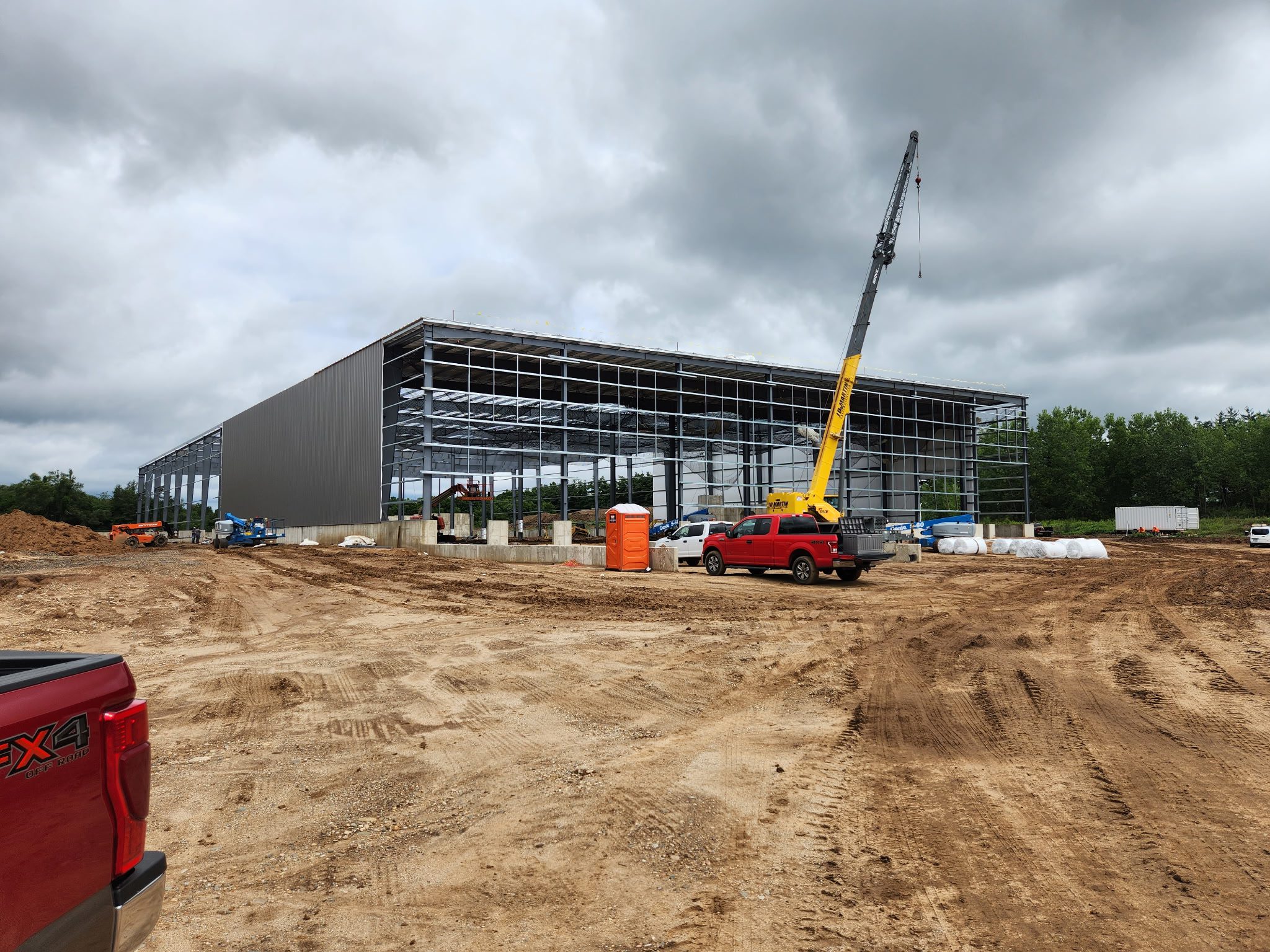 Construction site with steel framework and crane under cloudy sky.