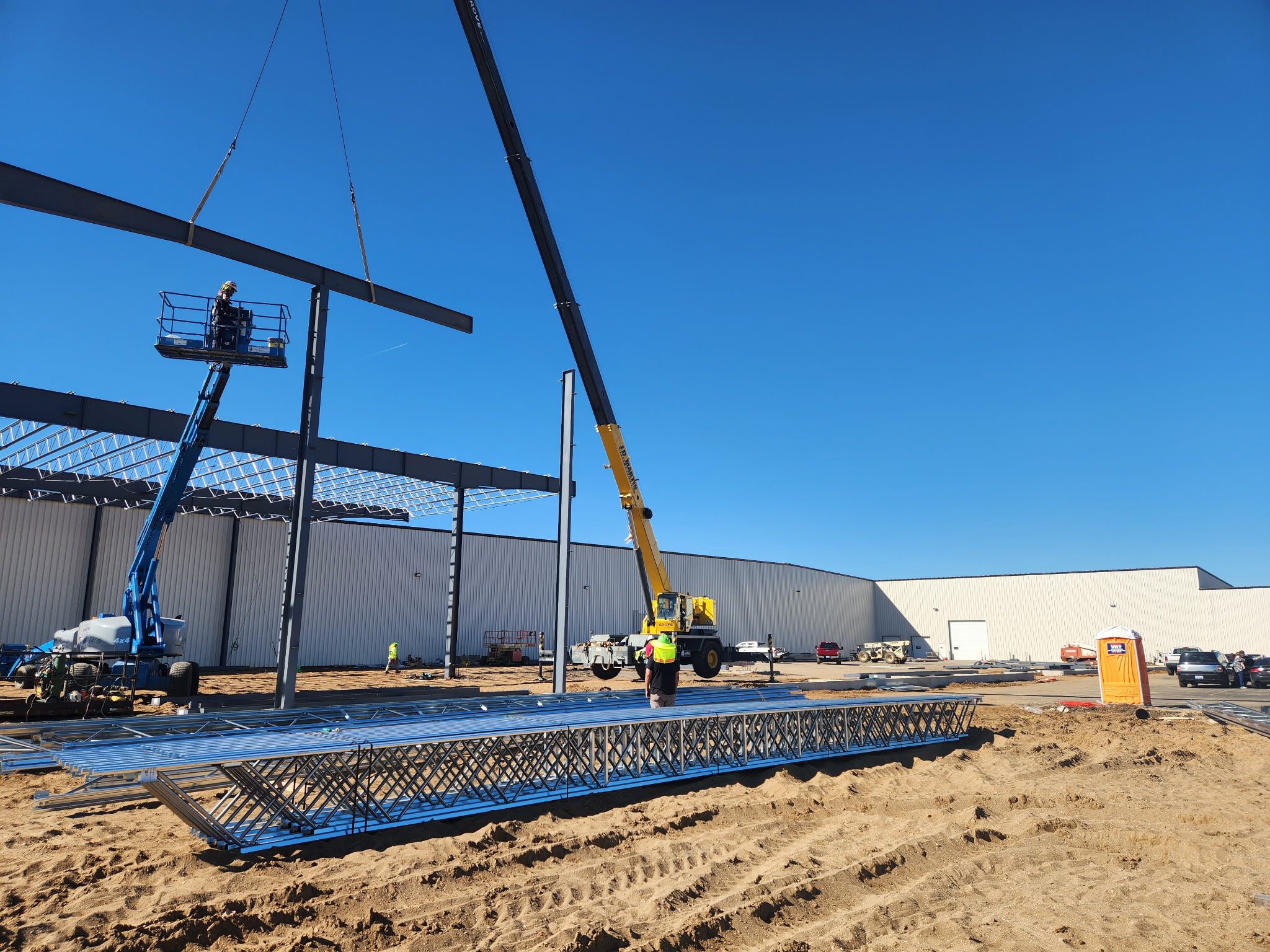 Construction workers using a crane to install steel beams at a building site.
