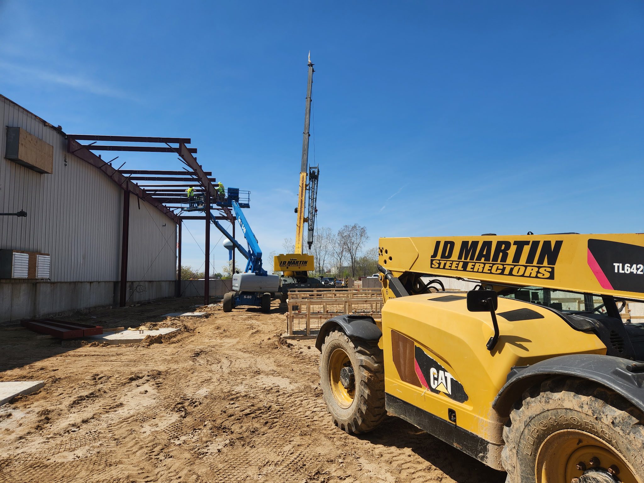 Construction vehicles at a building site under clear blue sky.