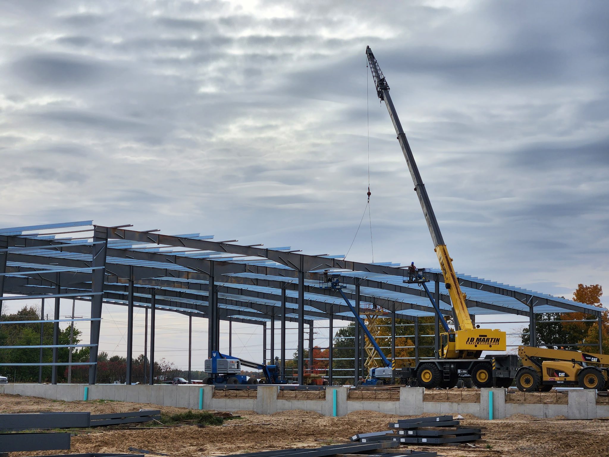 A crane lifting materials at a steel frame construction site under cloudy sky.