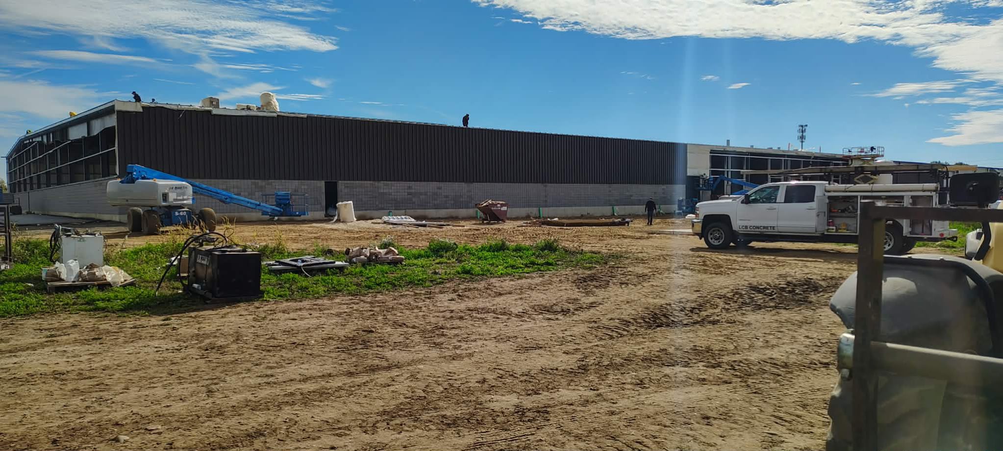Construction site with dirt ground and a large building under blue sky.