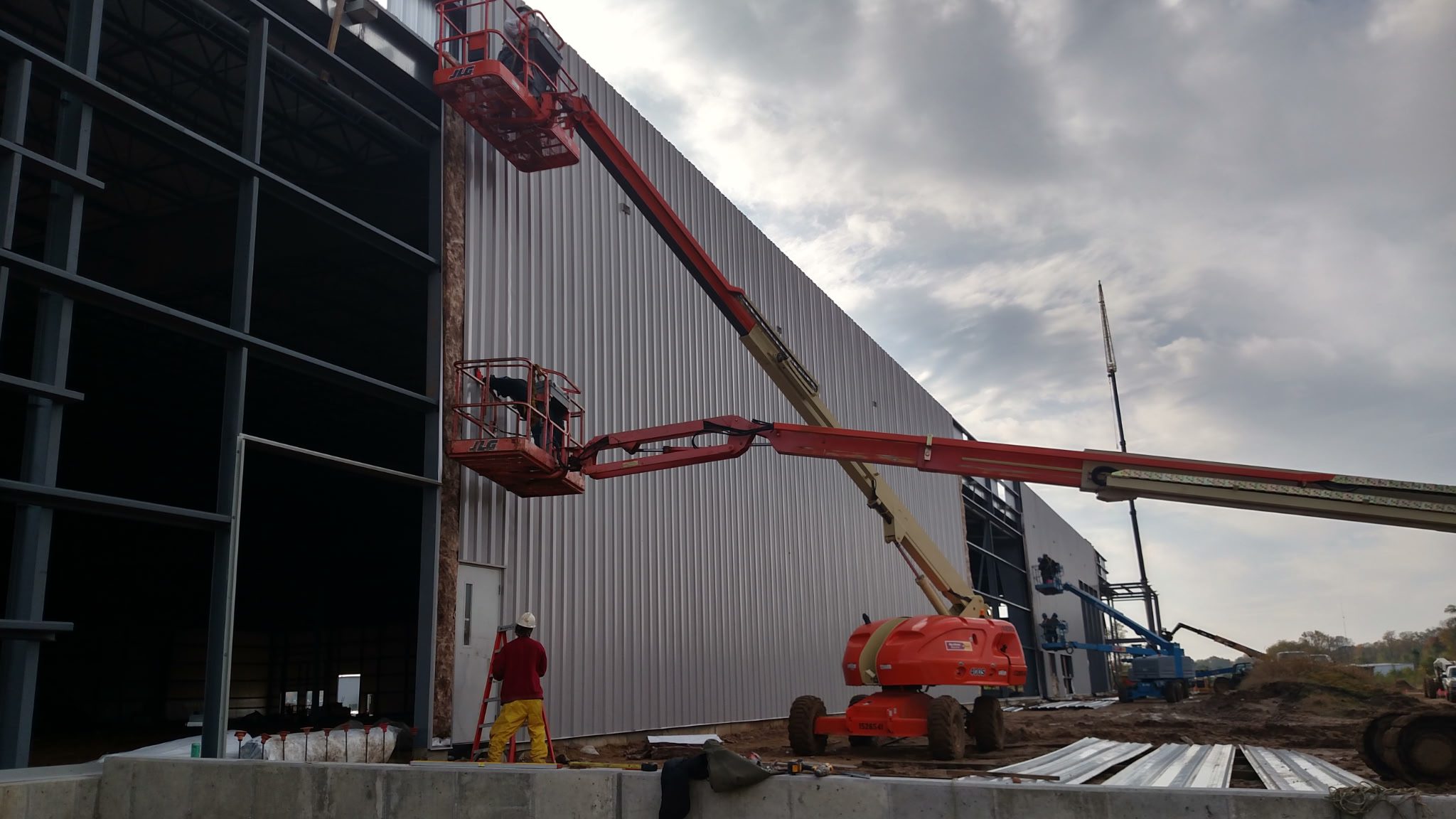 Construction workers operate boom lifts on a building exterior under a cloudy sky.