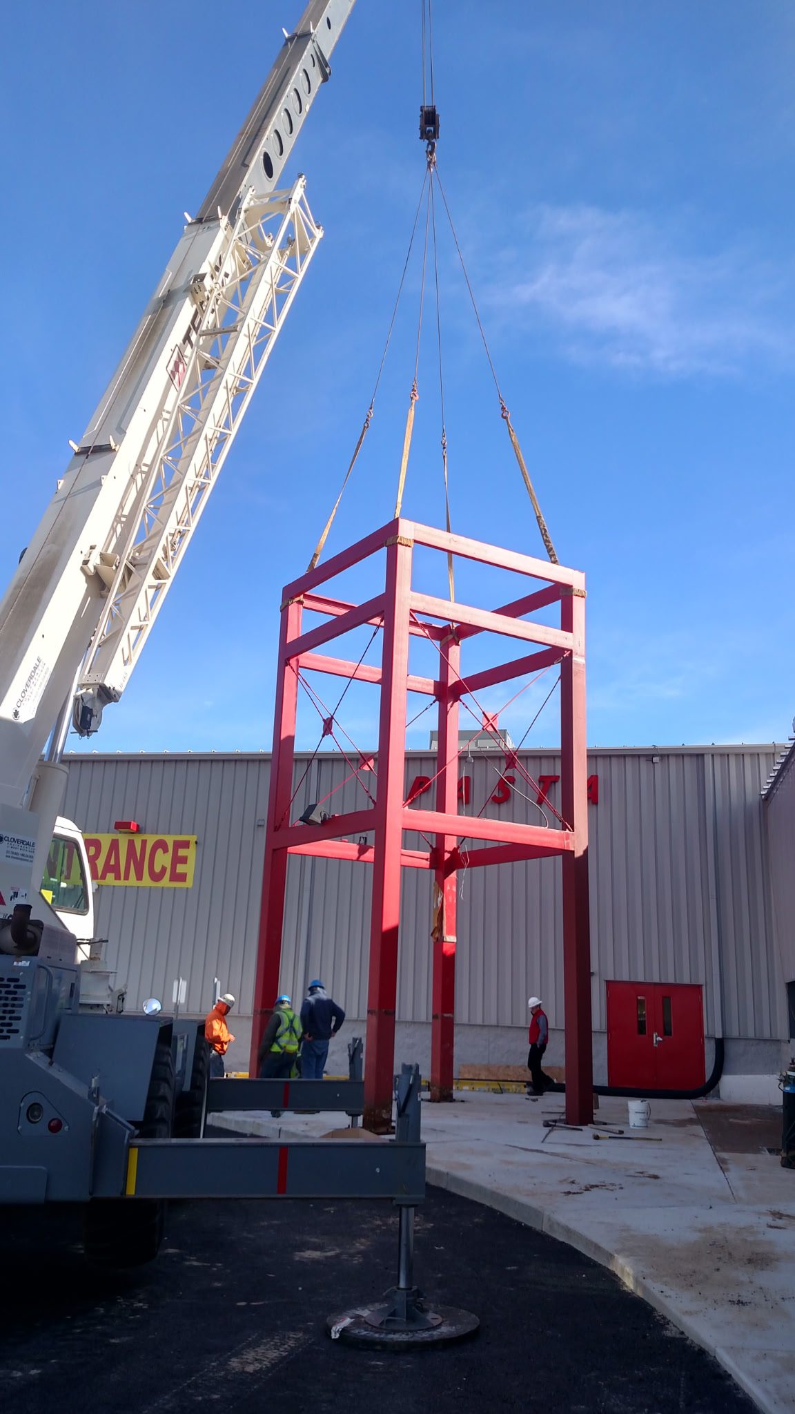 A red metal structure being lifted by a crane outdoors.