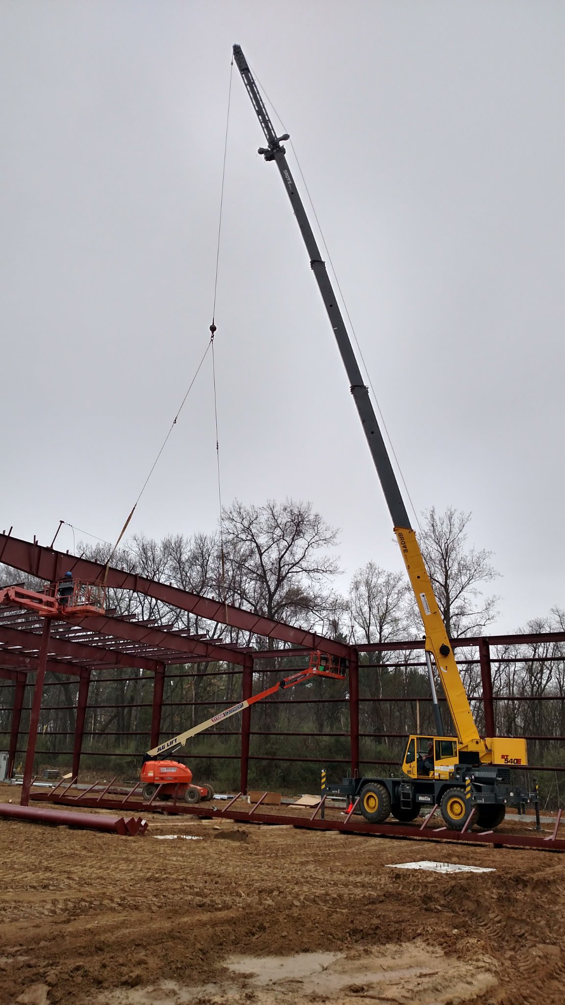 Crane lifting a steel beam on a construction site under cloudy sky.