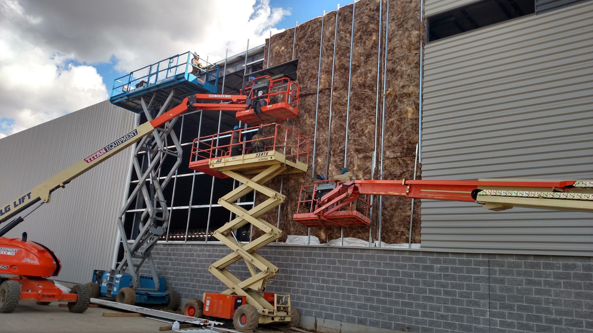 Workers installing large panels on a building exterior using lifts.