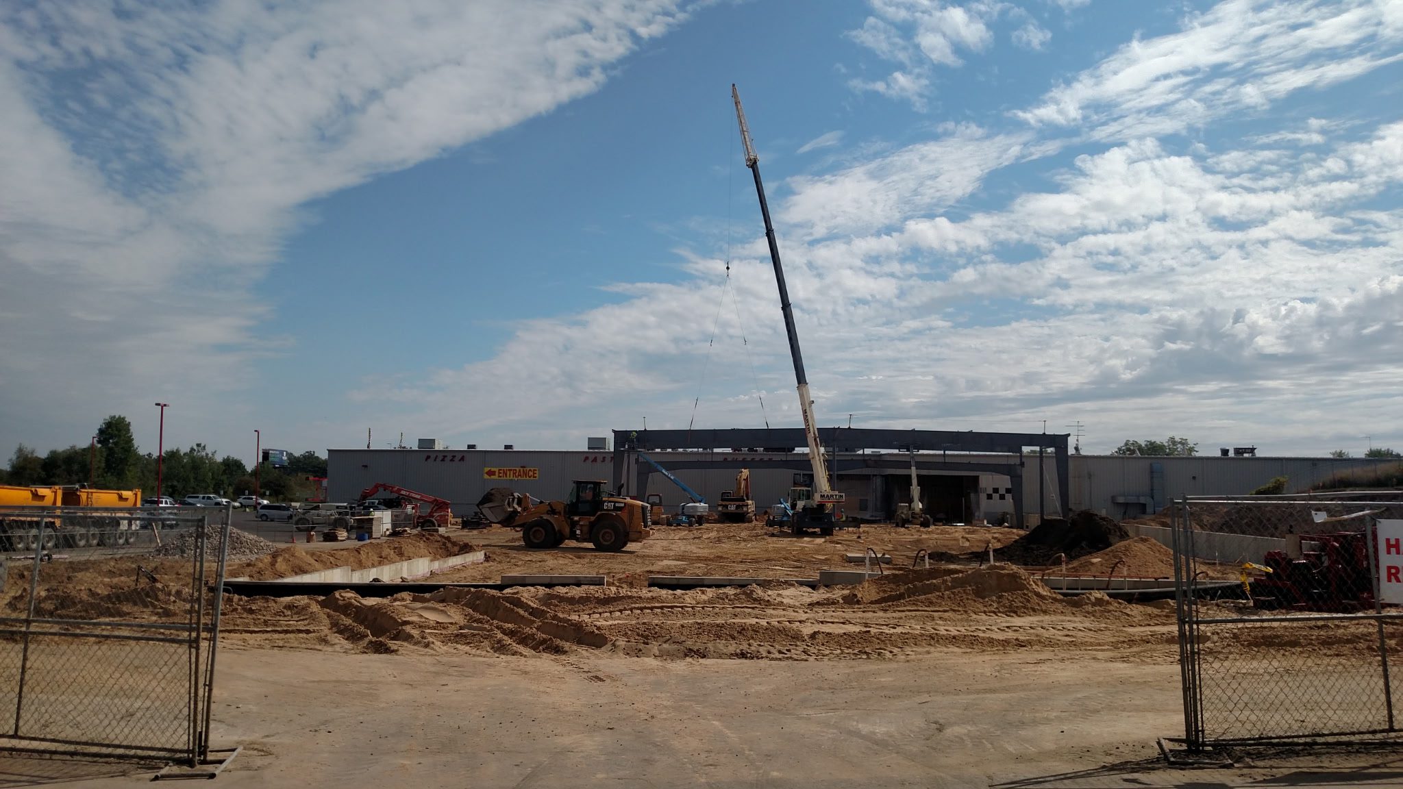 Construction site with a crane lifting materials near a building under a partly cloudy sky.