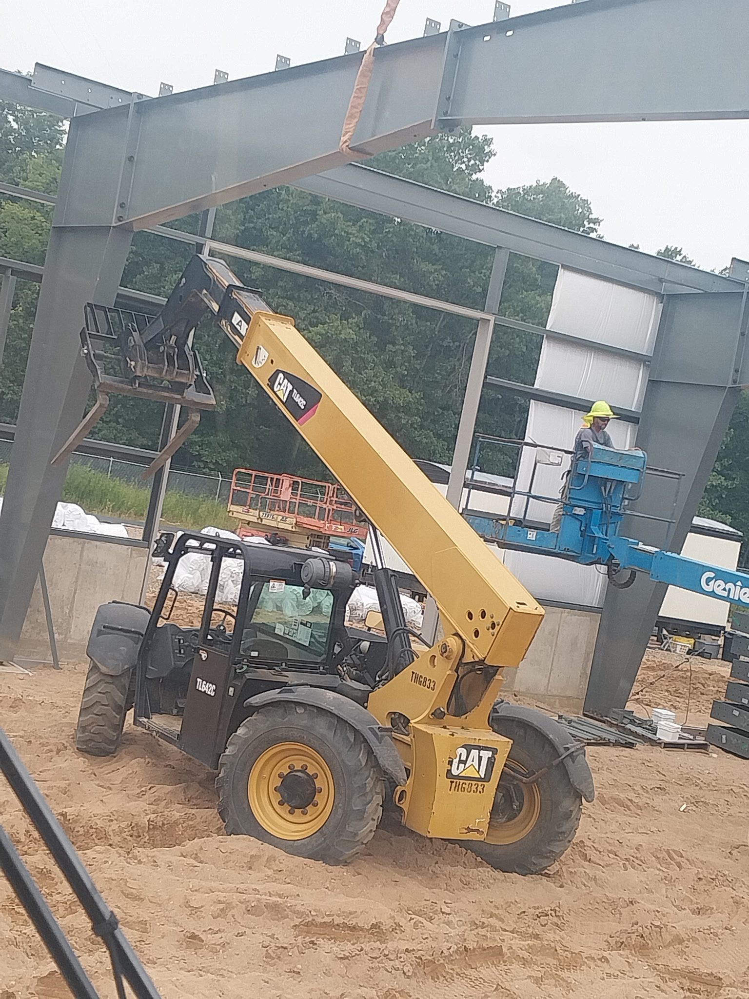 A yellow telescopic handler lifting a pallet at a construction site.