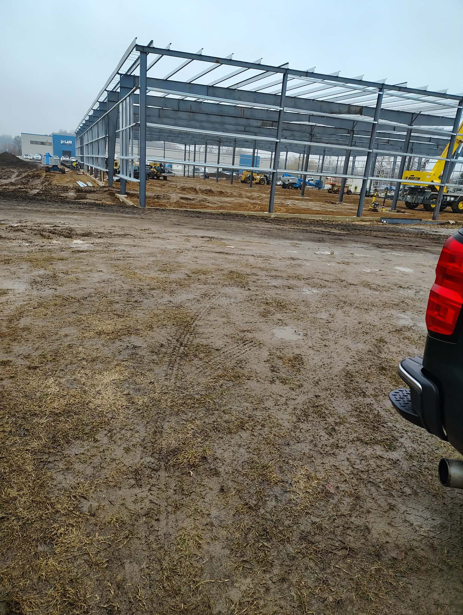 Construction site with steel framework and muddy ground under overcast sky.