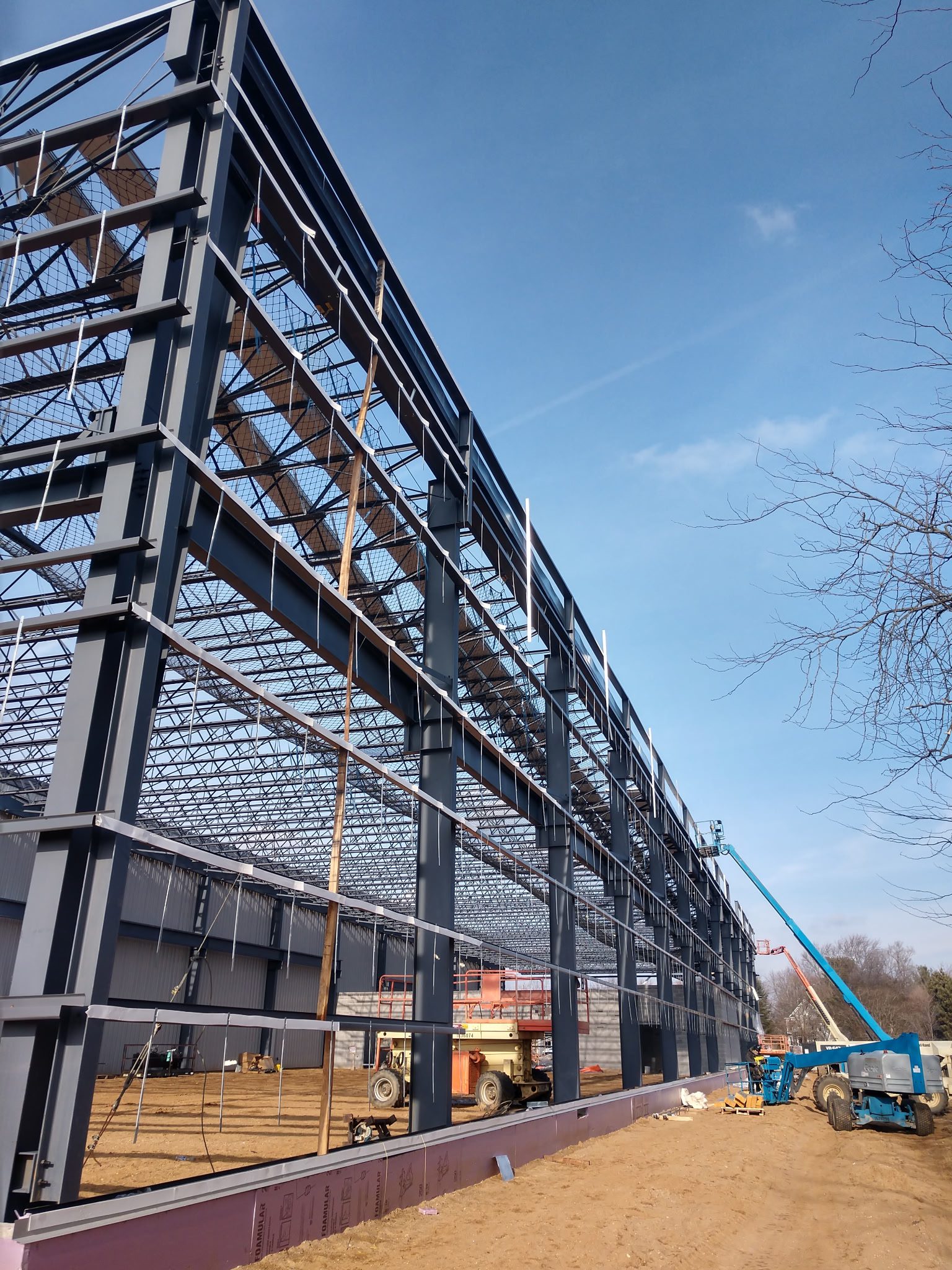 Construction workers building a large steel framework under a clear sky.