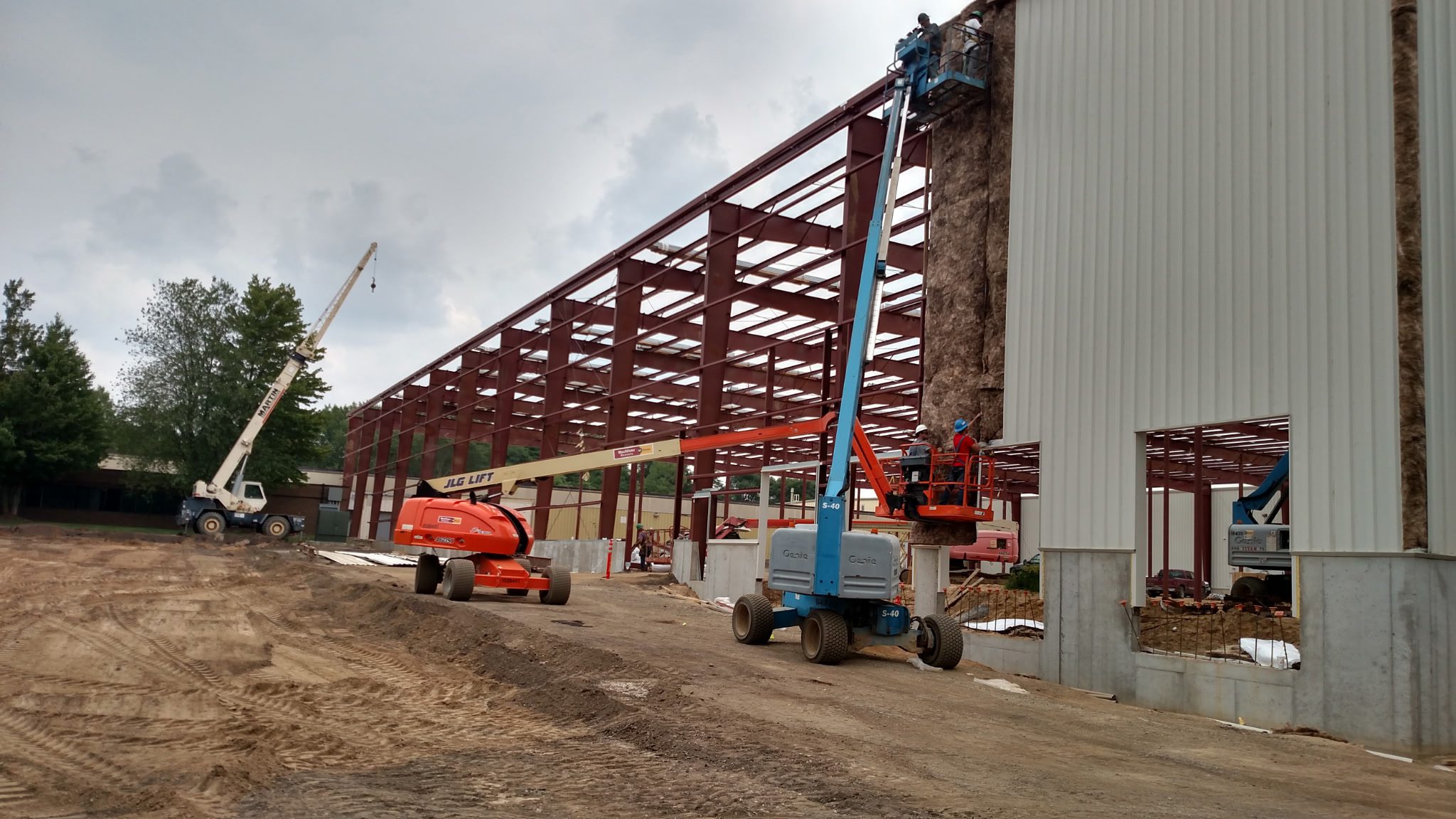Construction site with steel framework and two aerial lifts.