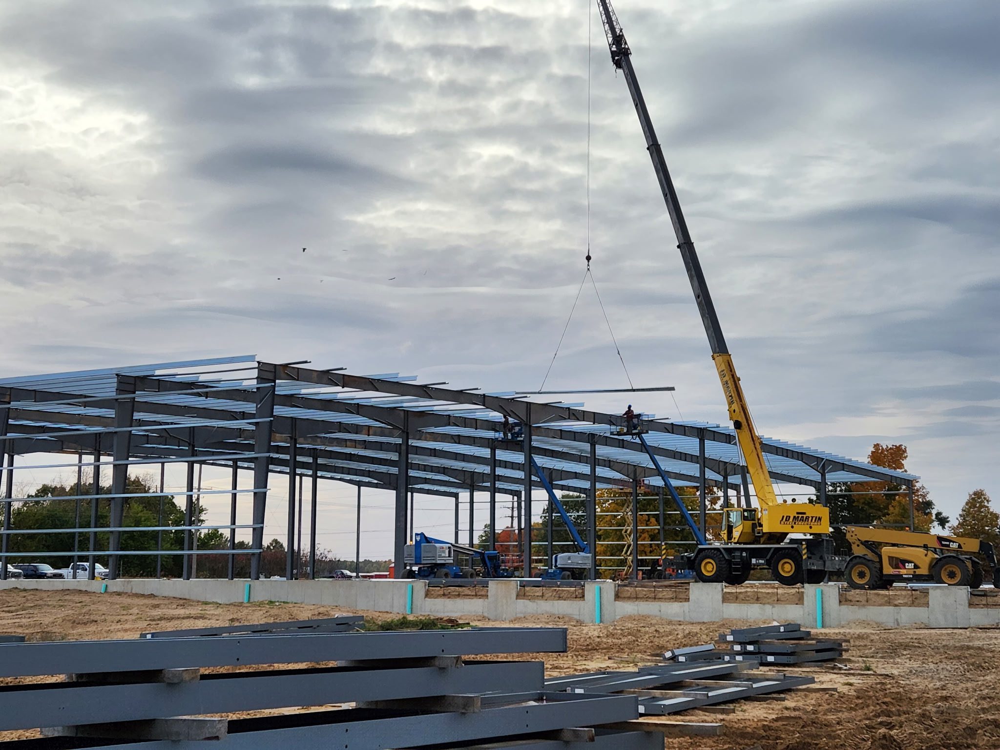 Crane lifting materials at a construction site with steel framework under a cloudy sky.