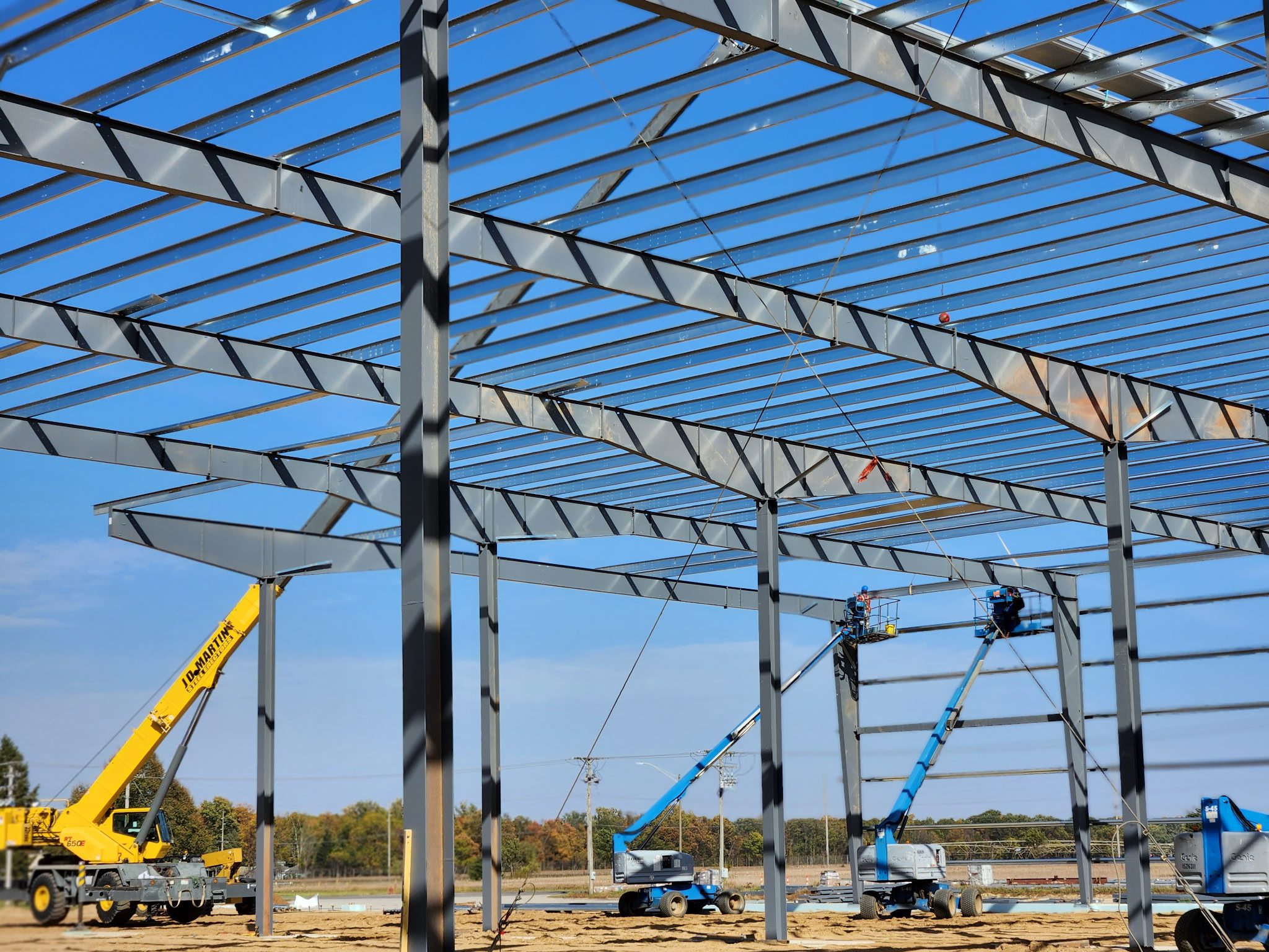 Steel framework of a building under construction with cranes in the background.