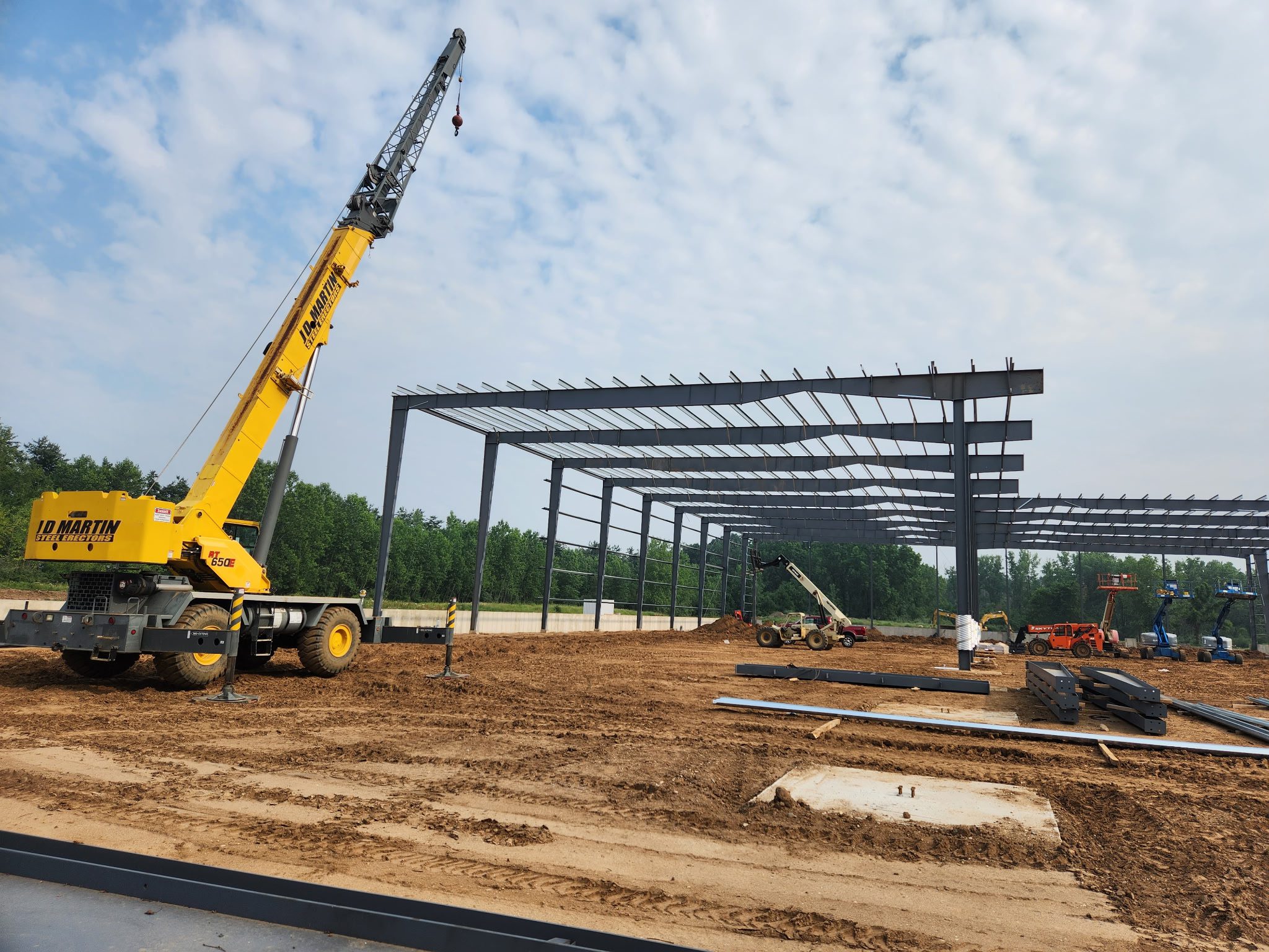Construction site with steel framework and a yellow crane under a partly cloudy sky.
