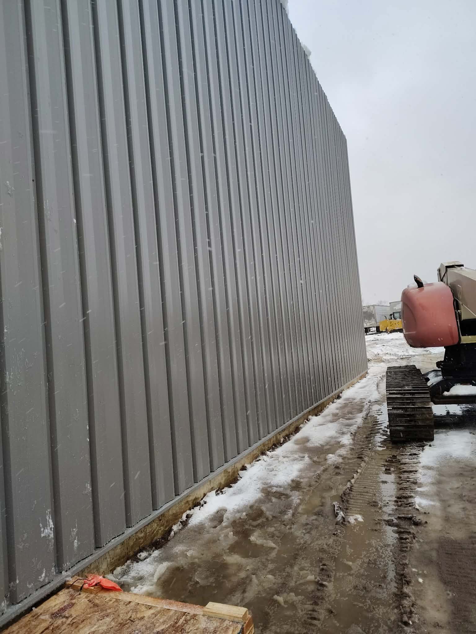Construction site with a metal fence and machinery in snowy conditions.
