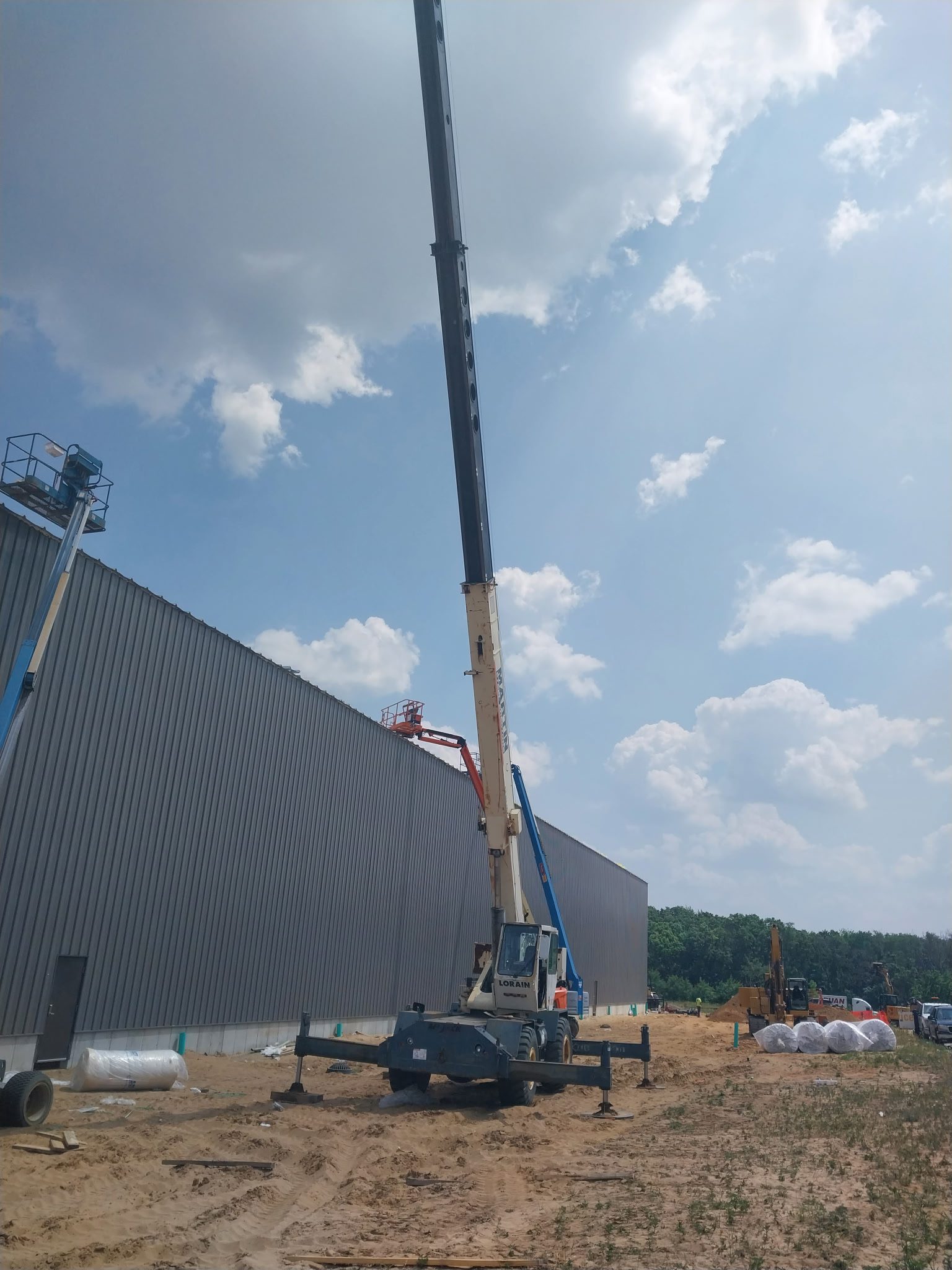 A crane lifting a large industrial panel near a building under a partly cloudy sky.