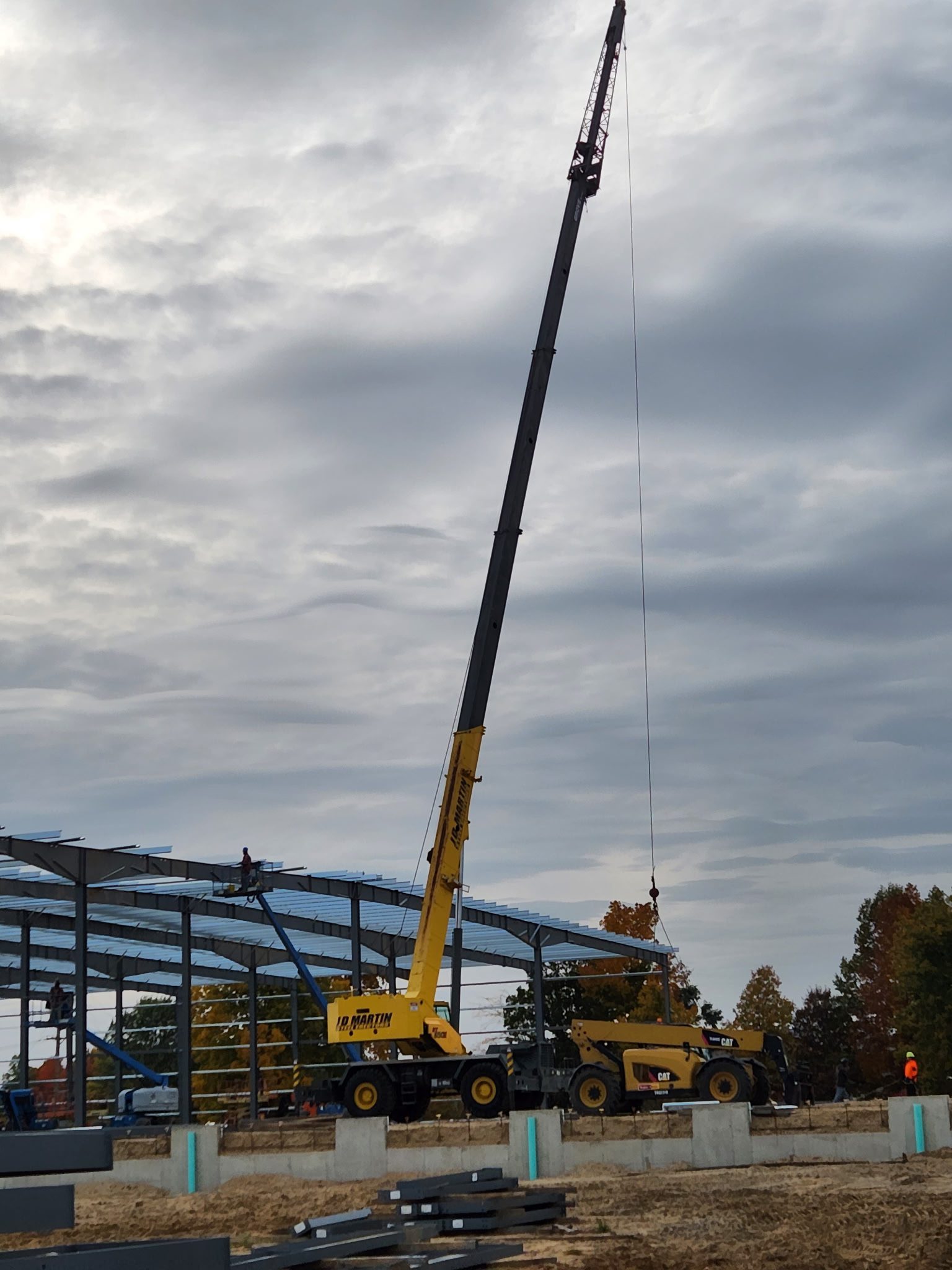 A crane lifting materials at a construction site with a cloudy sky.