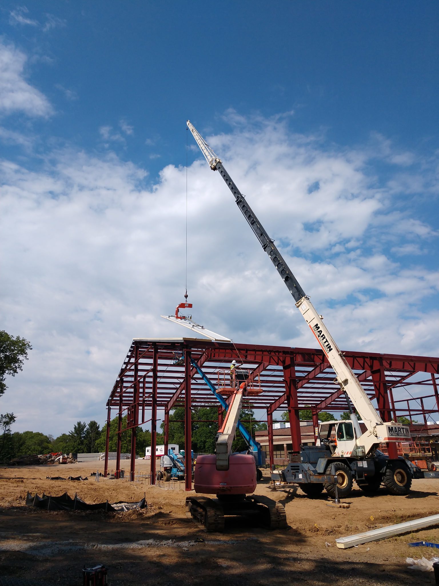 Crane lifting steel beams at a construction site under a blue sky.