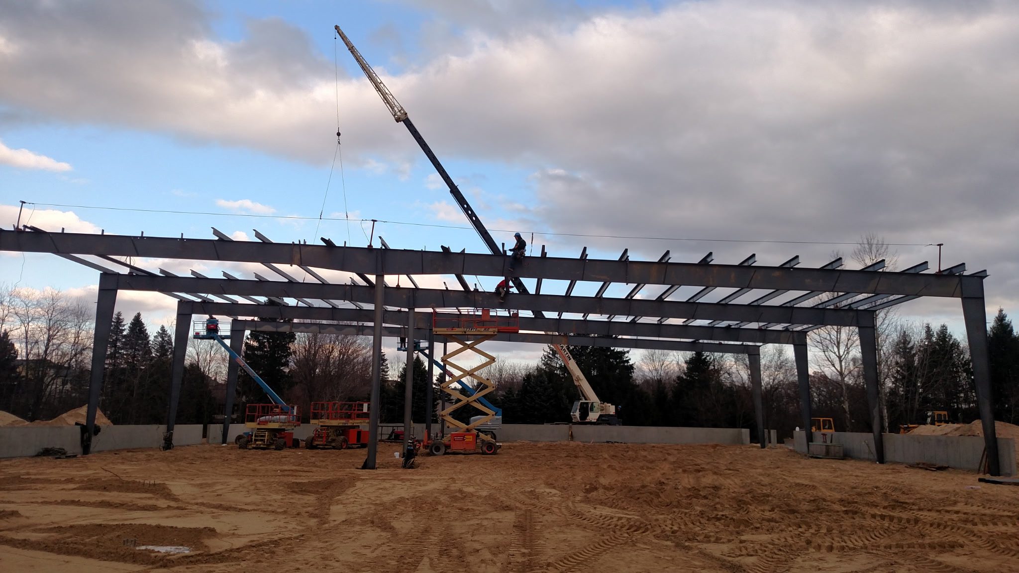 Crane lifting steel beams at a construction site under a cloudy sky.