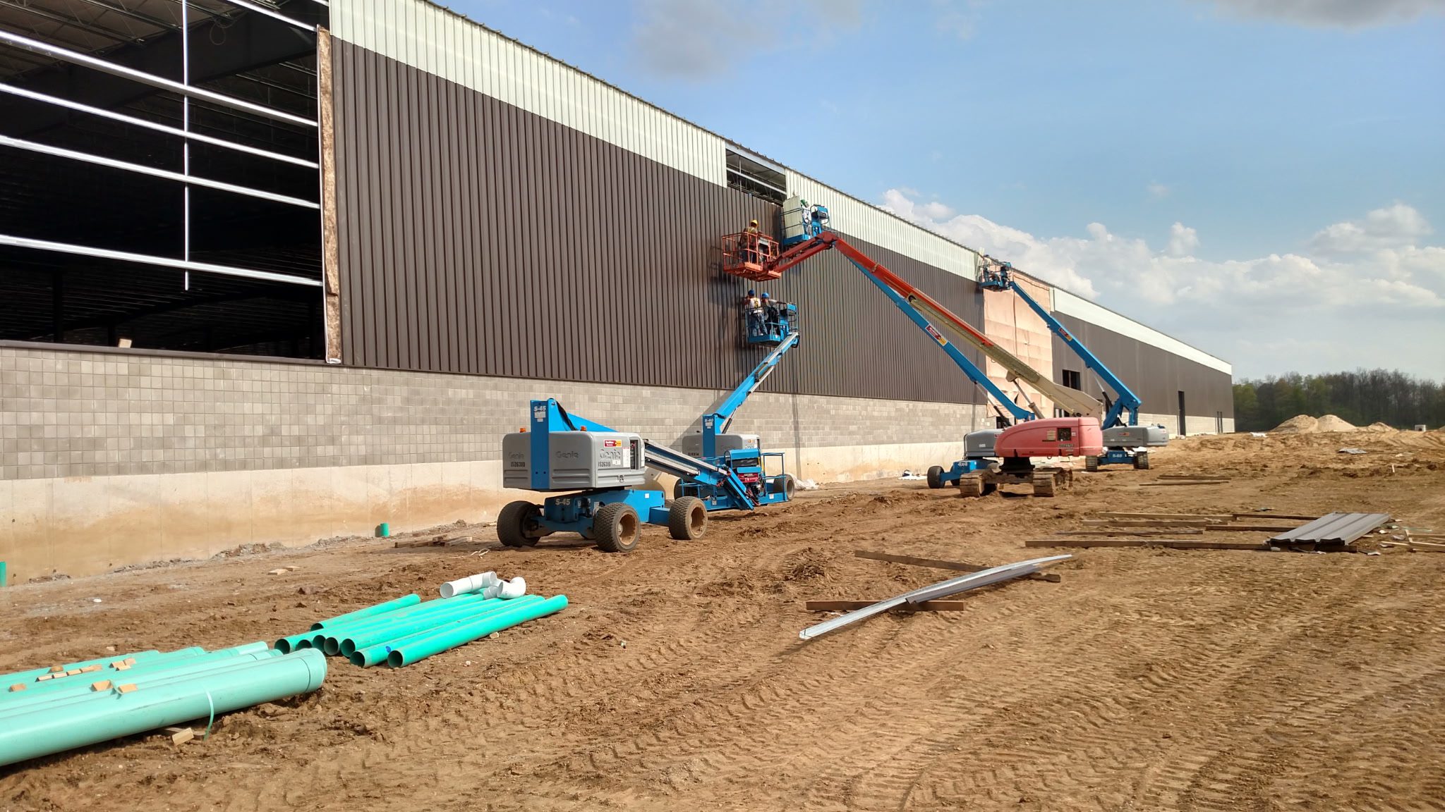 Construction workers using boom lifts to work on a large building wall.