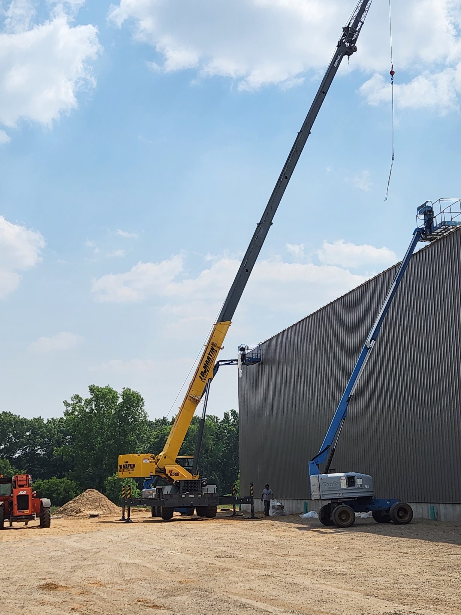 Two cranes lifting materials onto a tall building under a partly cloudy sky.