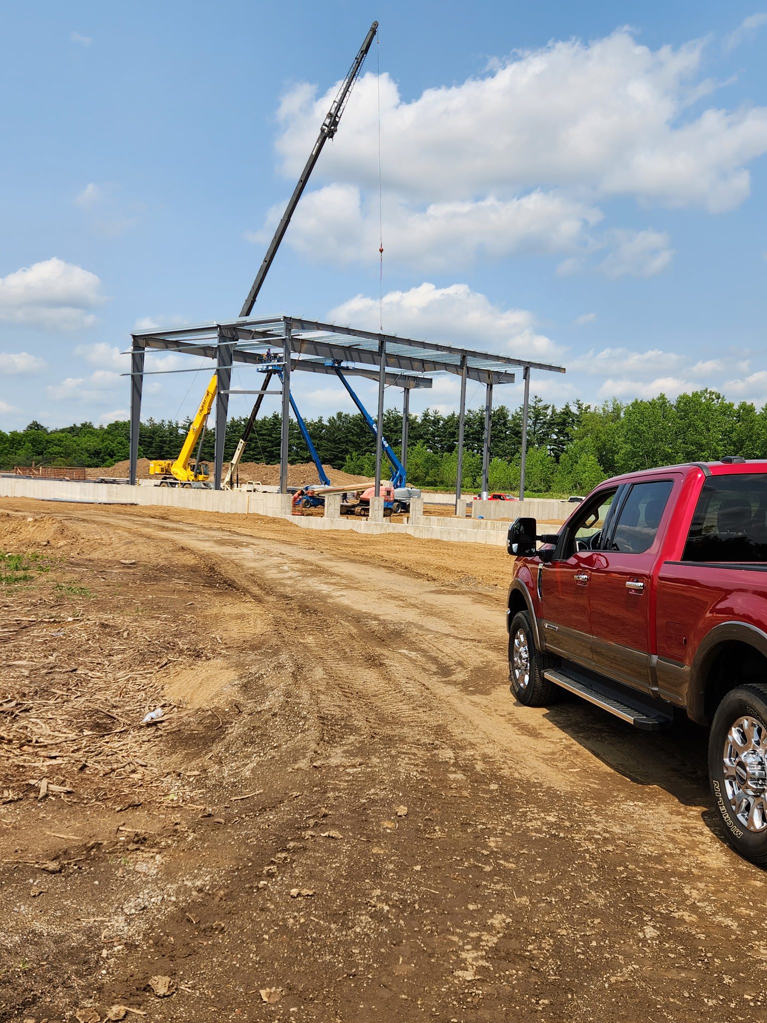 Construction of a steel structure with a red pickup truck nearby.