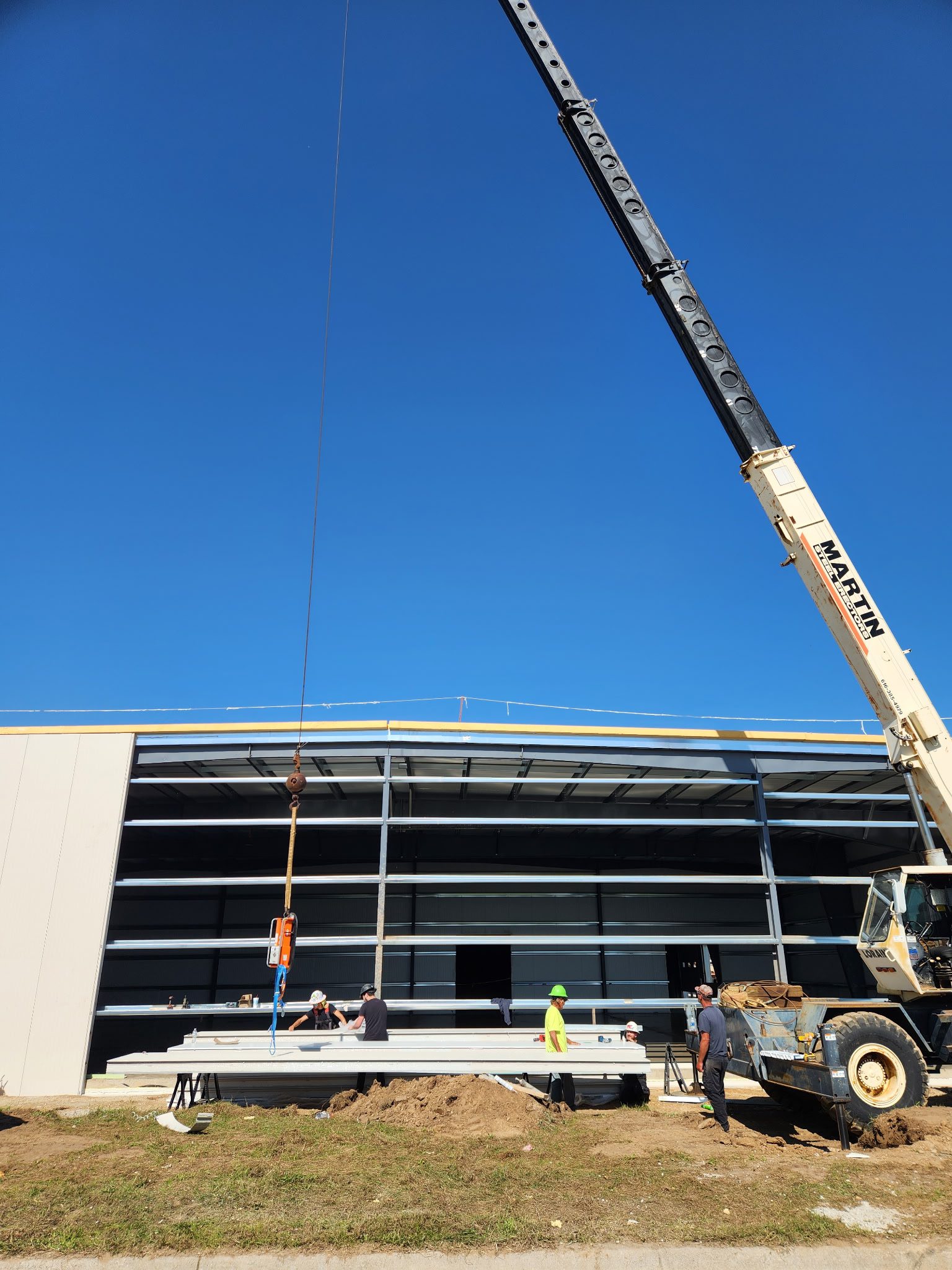 Construction crane lifting materials at a building site under clear blue sky.
