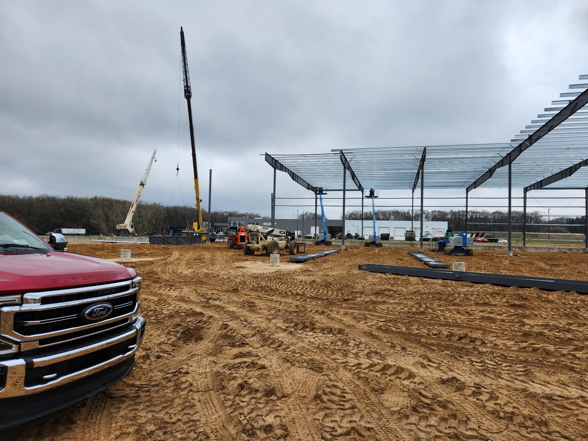 Construction site with steel framework and crane under cloudy sky.