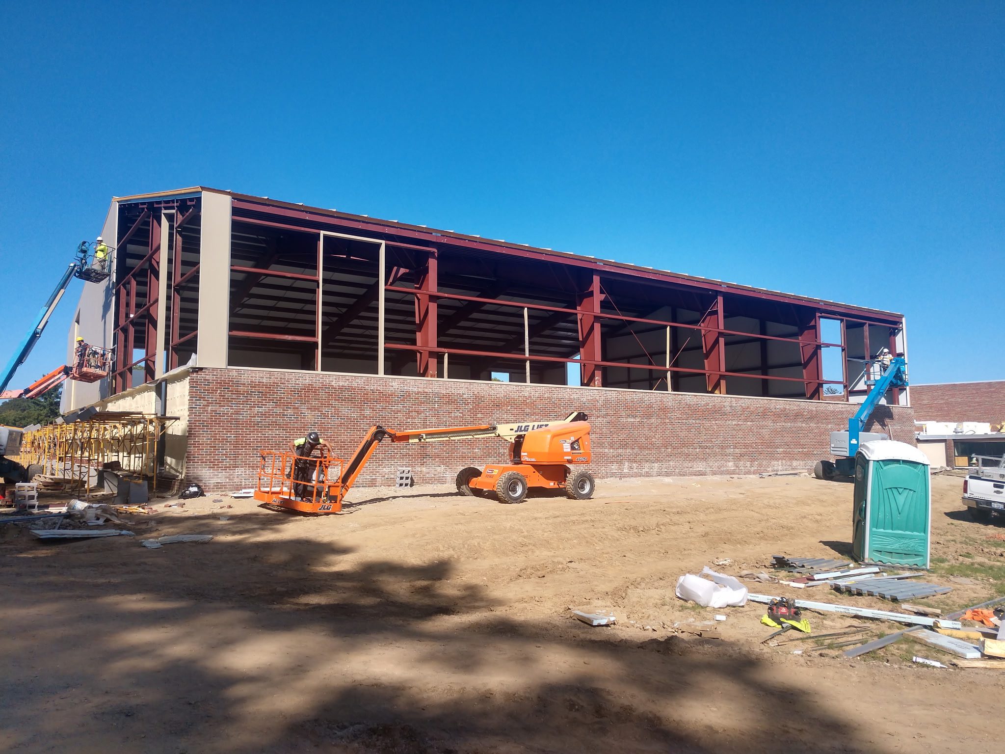 Construction site with workers building a brick structure under clear blue sky.
