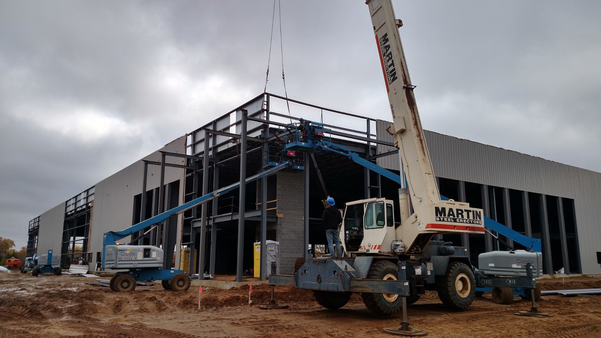 Construction site with crane lifting materials to steel building frame.