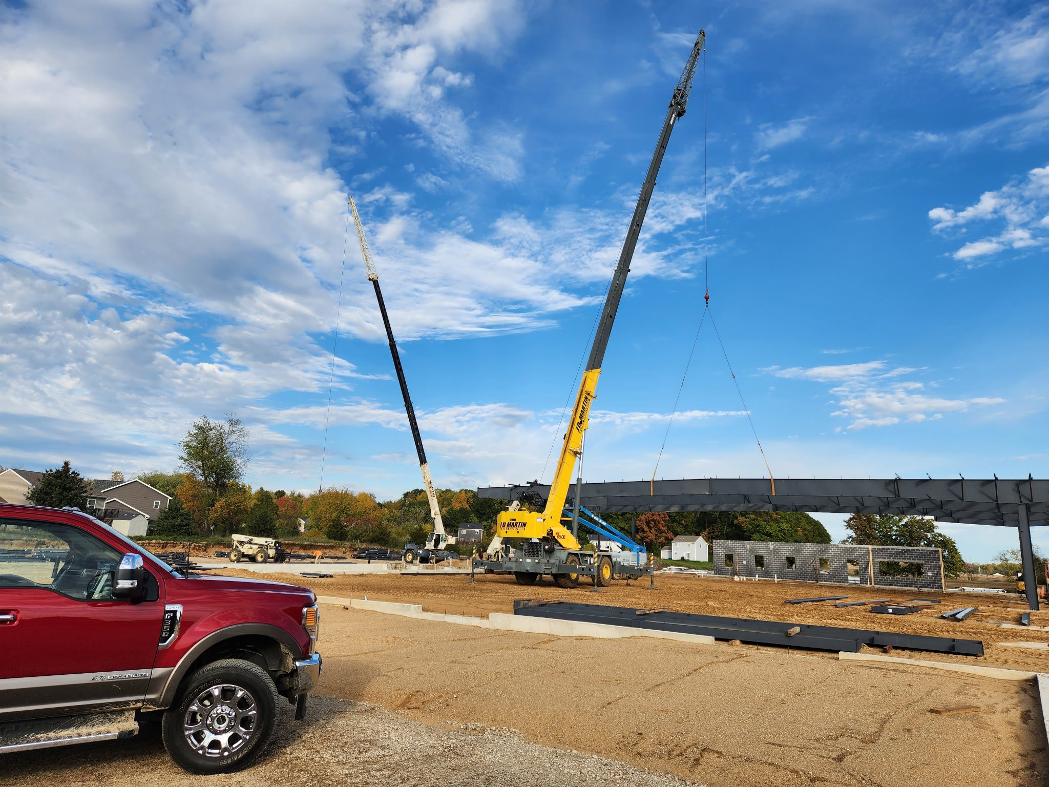 Two cranes lifting a large object at a construction site under a blue sky.