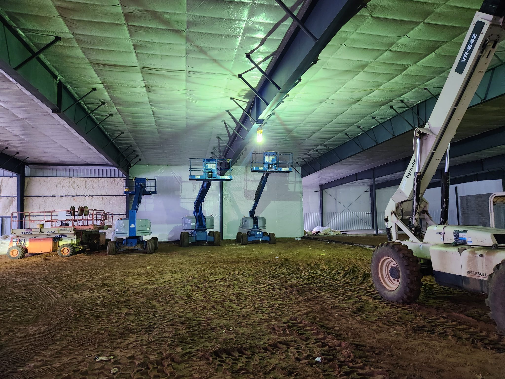 Two boom lifts inside a large indoor structure with grass floor.