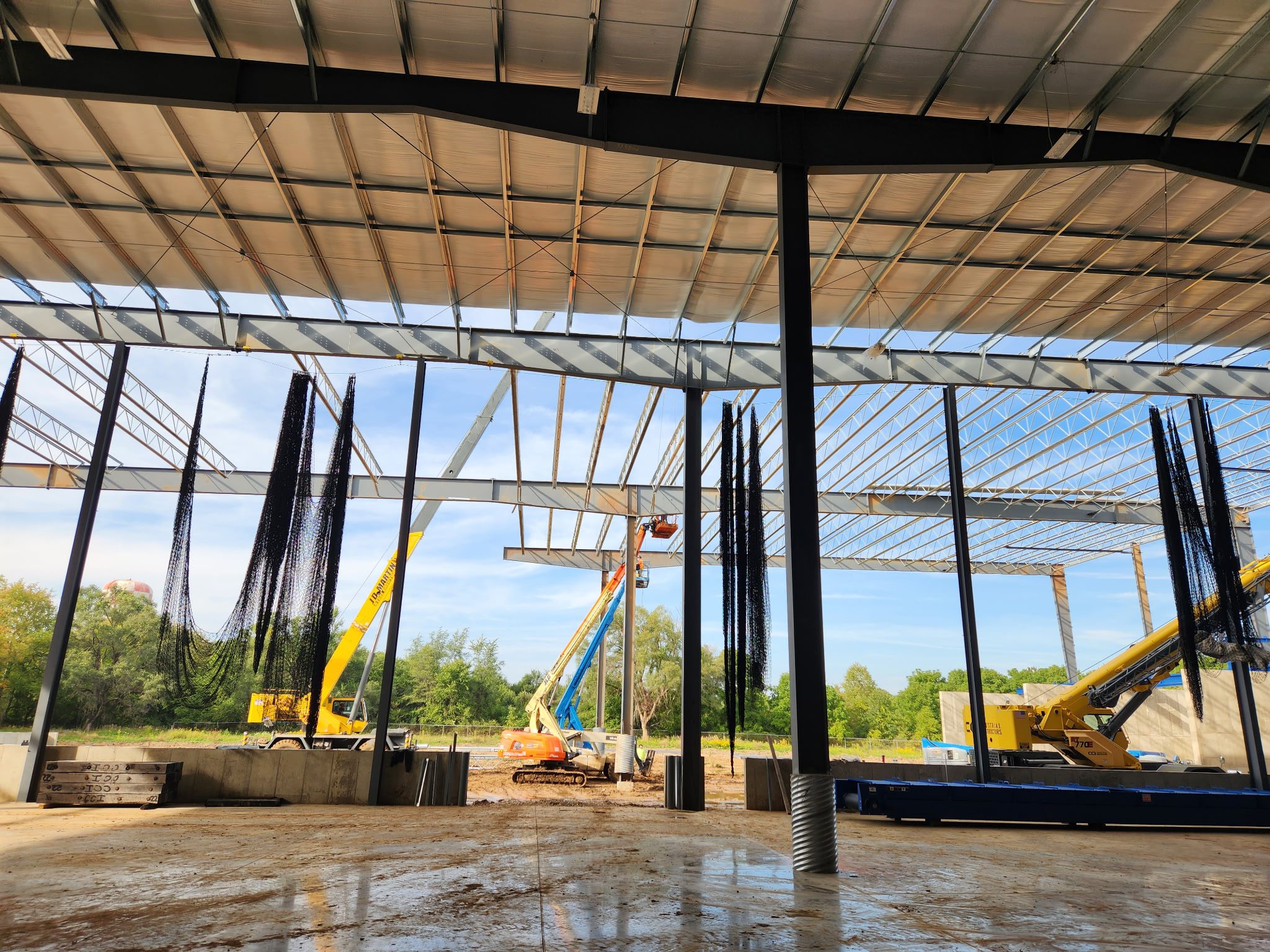 Construction site with steel framework and a crane under a metal roof.