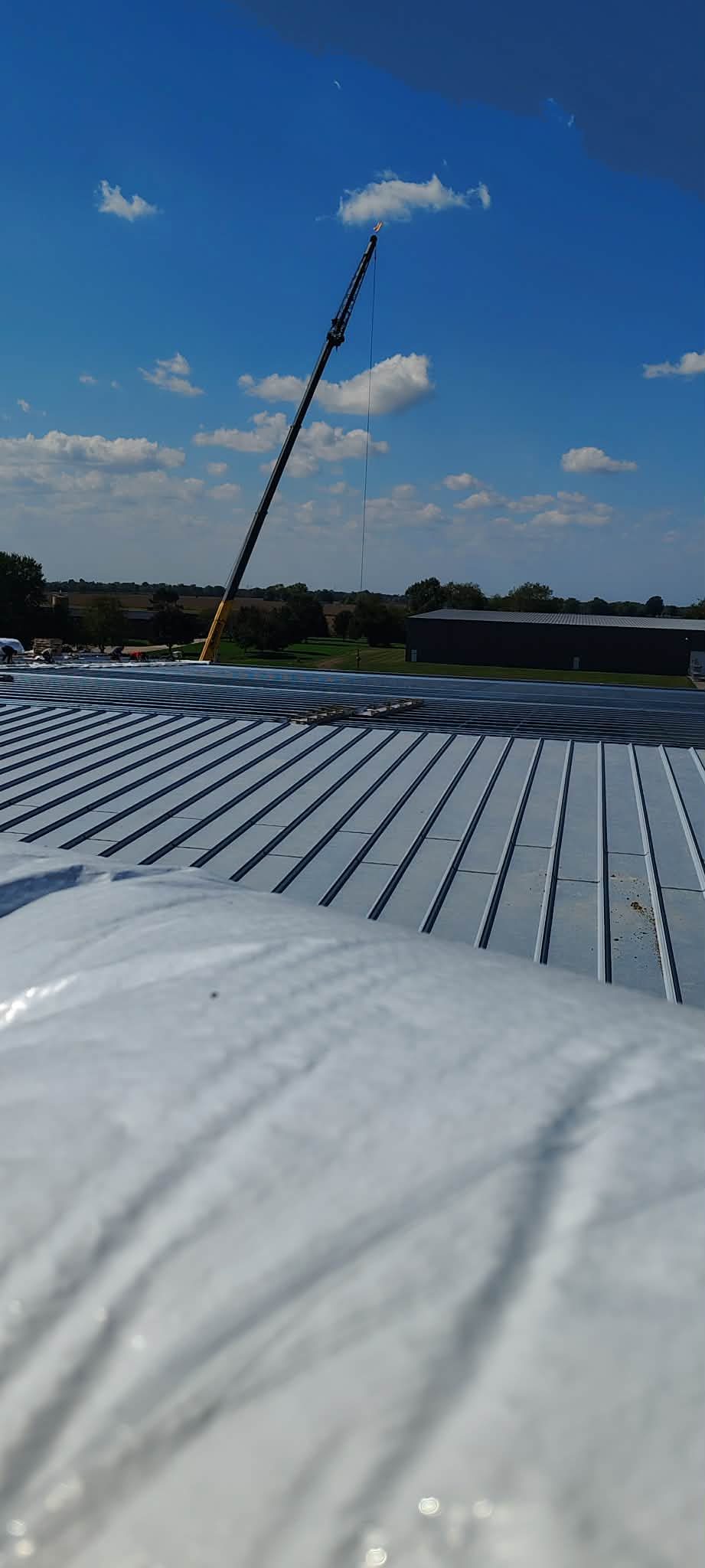 Close-up view of a metal roof under construction with a crane in the background.