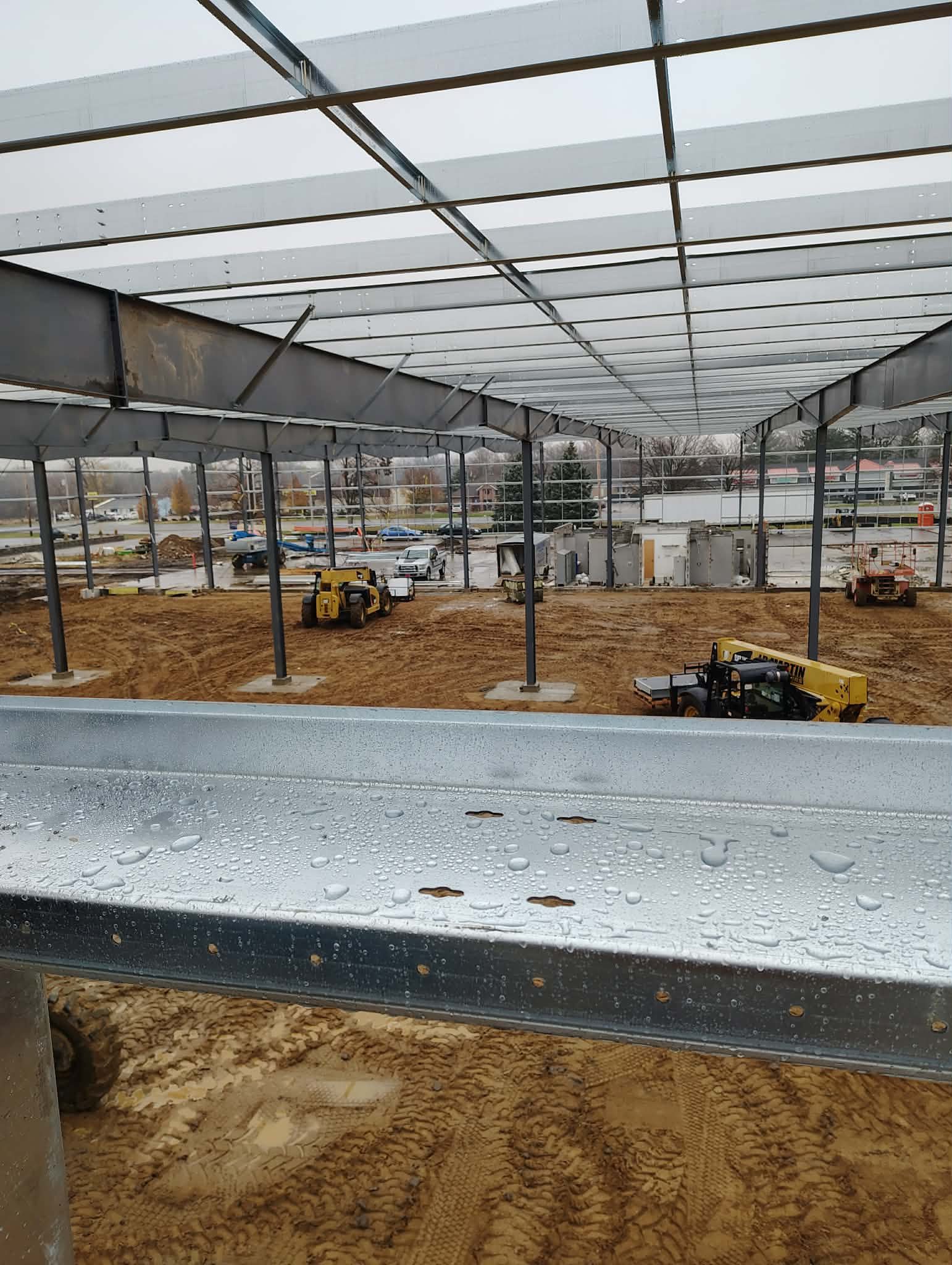 Construction site with machinery and steel beams under a large roof.