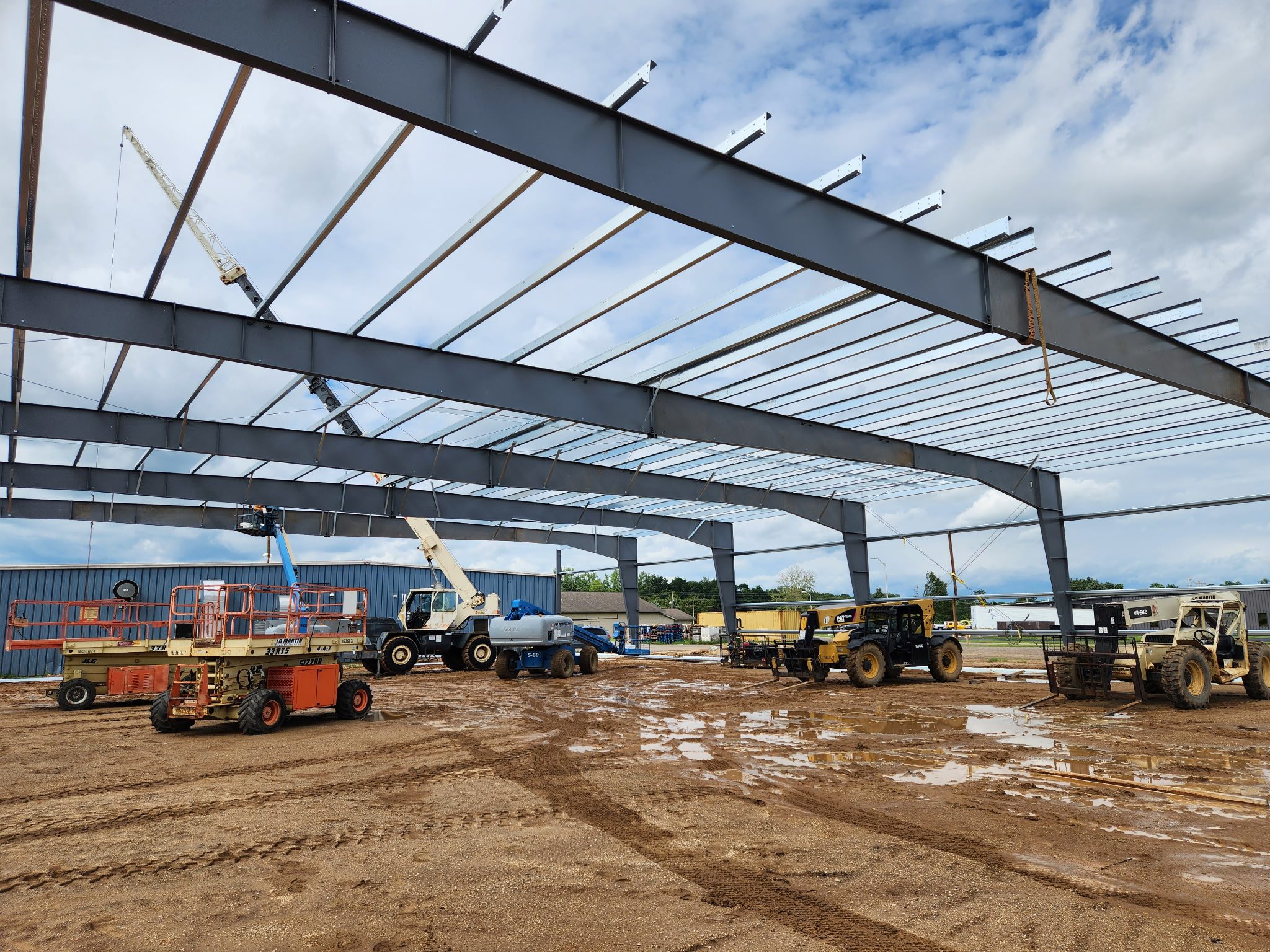 Steel framework being erected at a construction site under a blue sky.