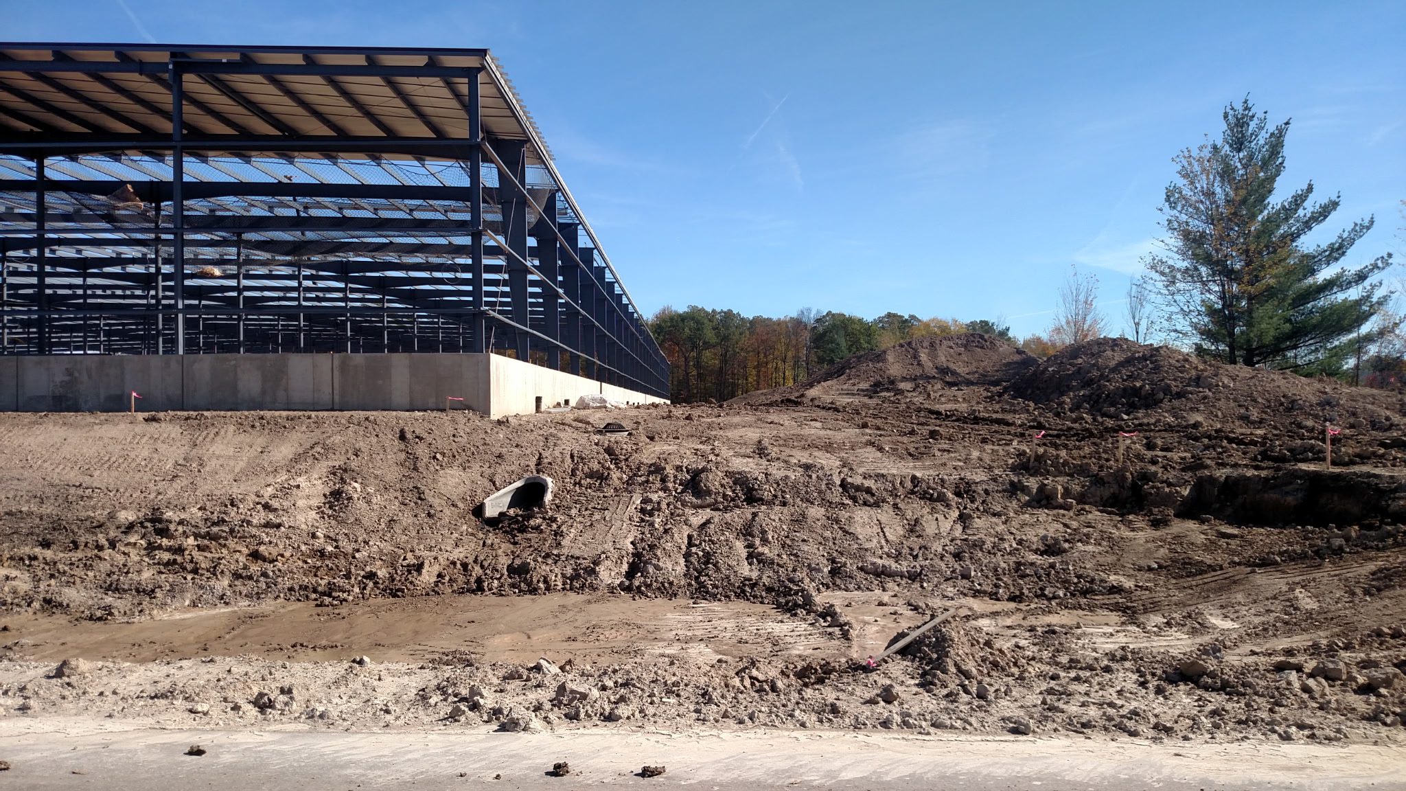 Construction site with steel framework and muddy ground under clear blue sky.