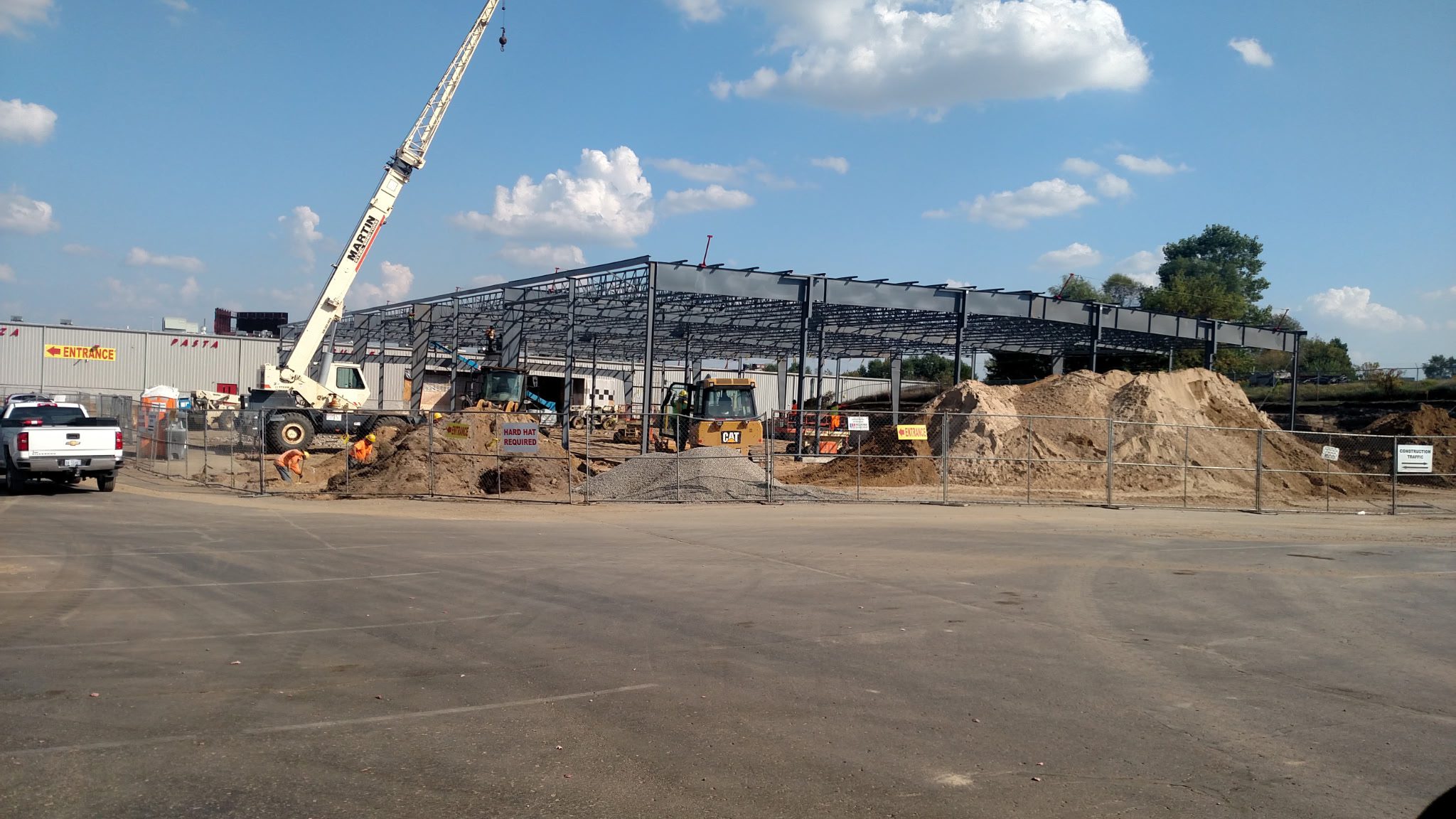Construction site with steel framework and crane under a blue sky.