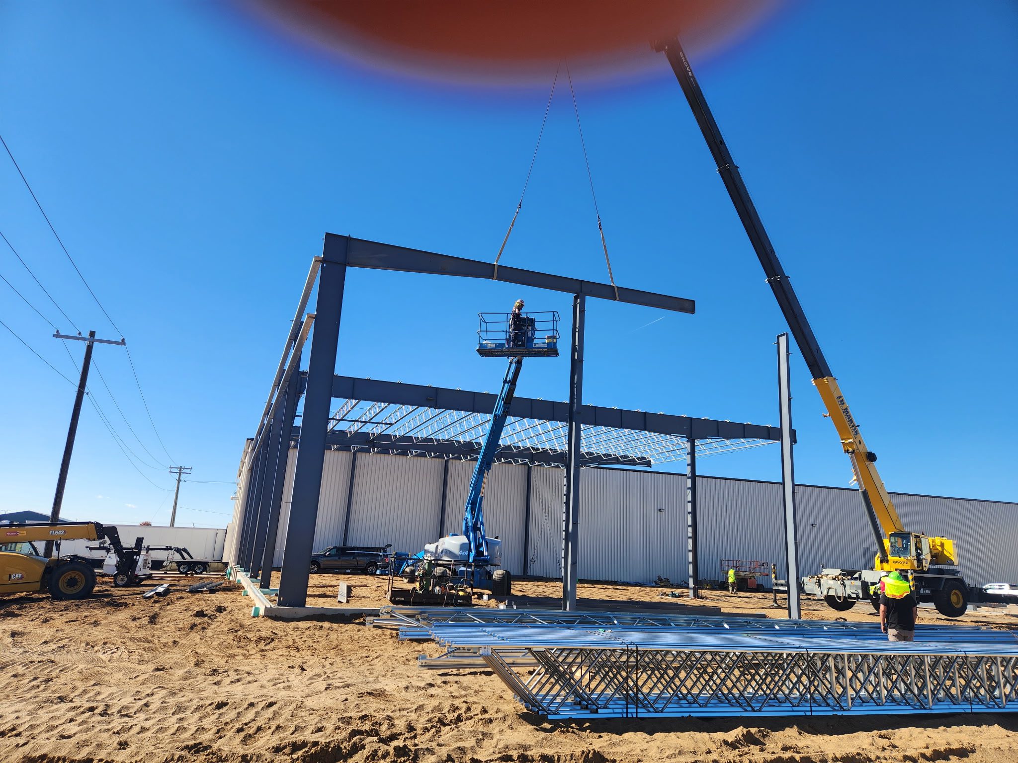 Construction site with steel framework and cranes under clear blue sky.